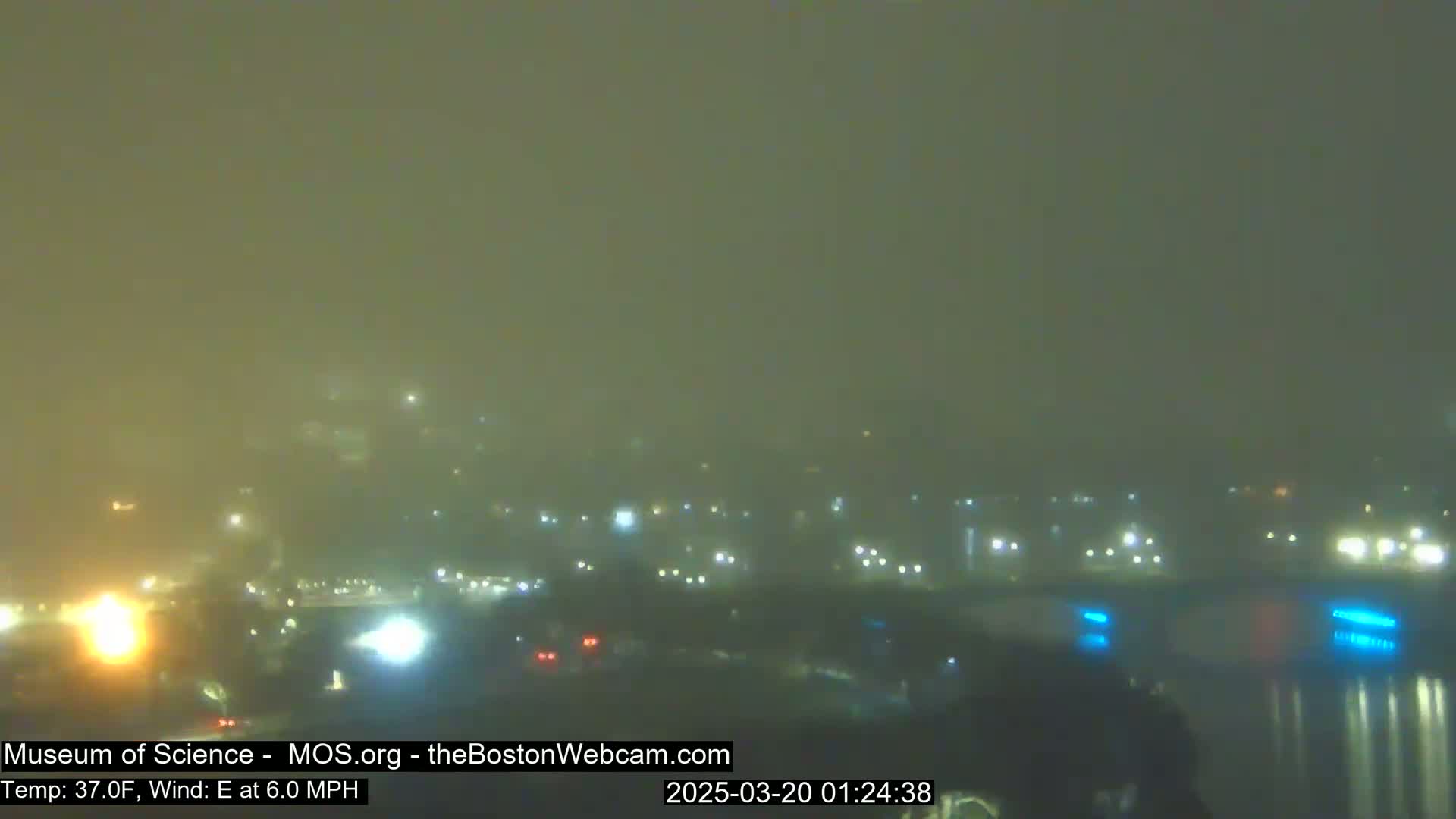 A foggy night scene shows a city skyline with distant lights and traffic faintly visible through the haze.