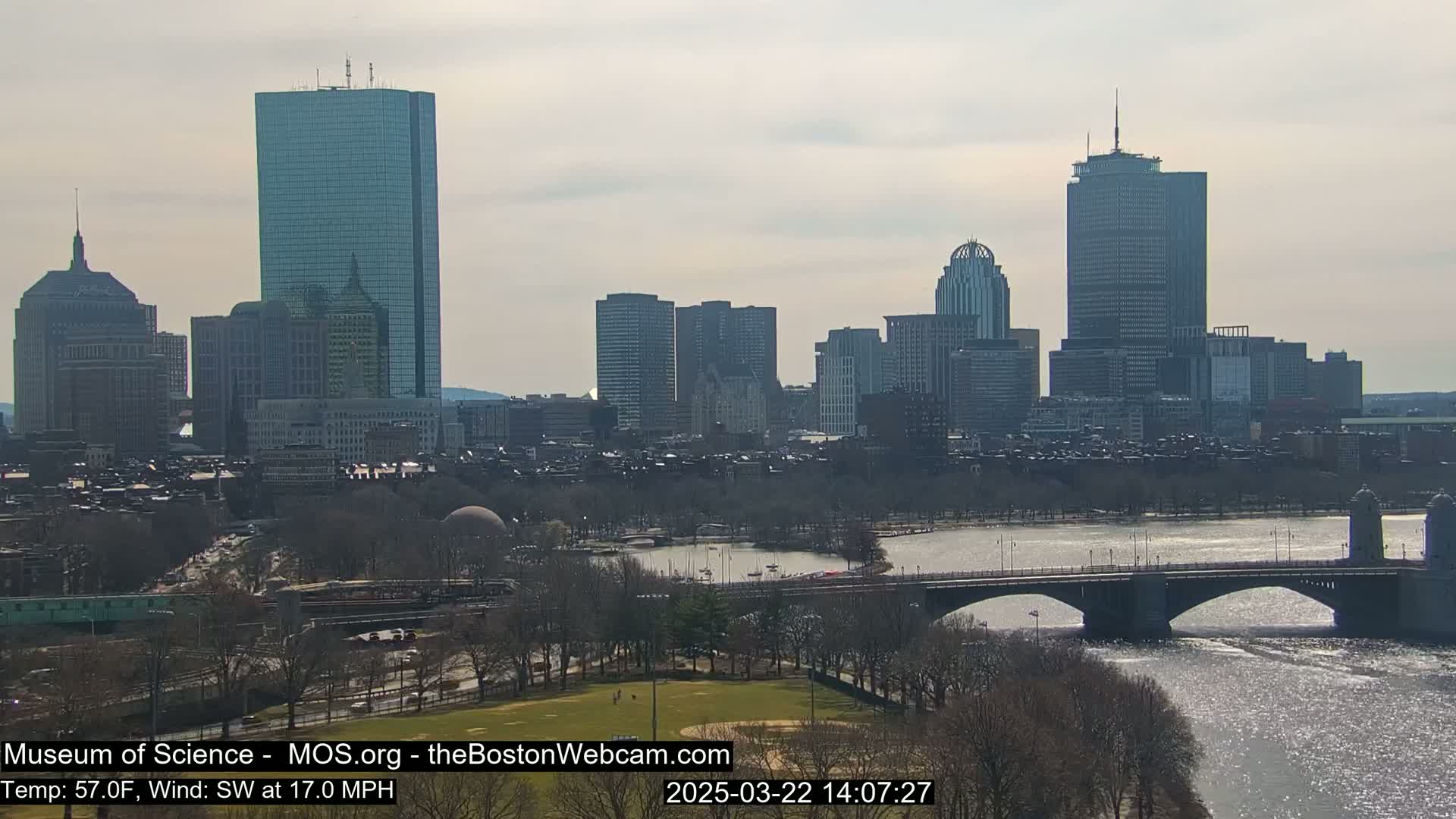 A cityscape with numerous skyscrapers and a river, under a partly cloudy sky, with a southwest wind at 17 mph and a temperature of 57°F.