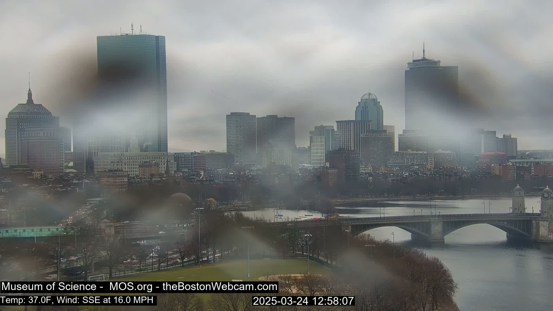 A hazy view of the Boston skyline, including a bridge over a river, on a cloudy day with a southeasterly wind.