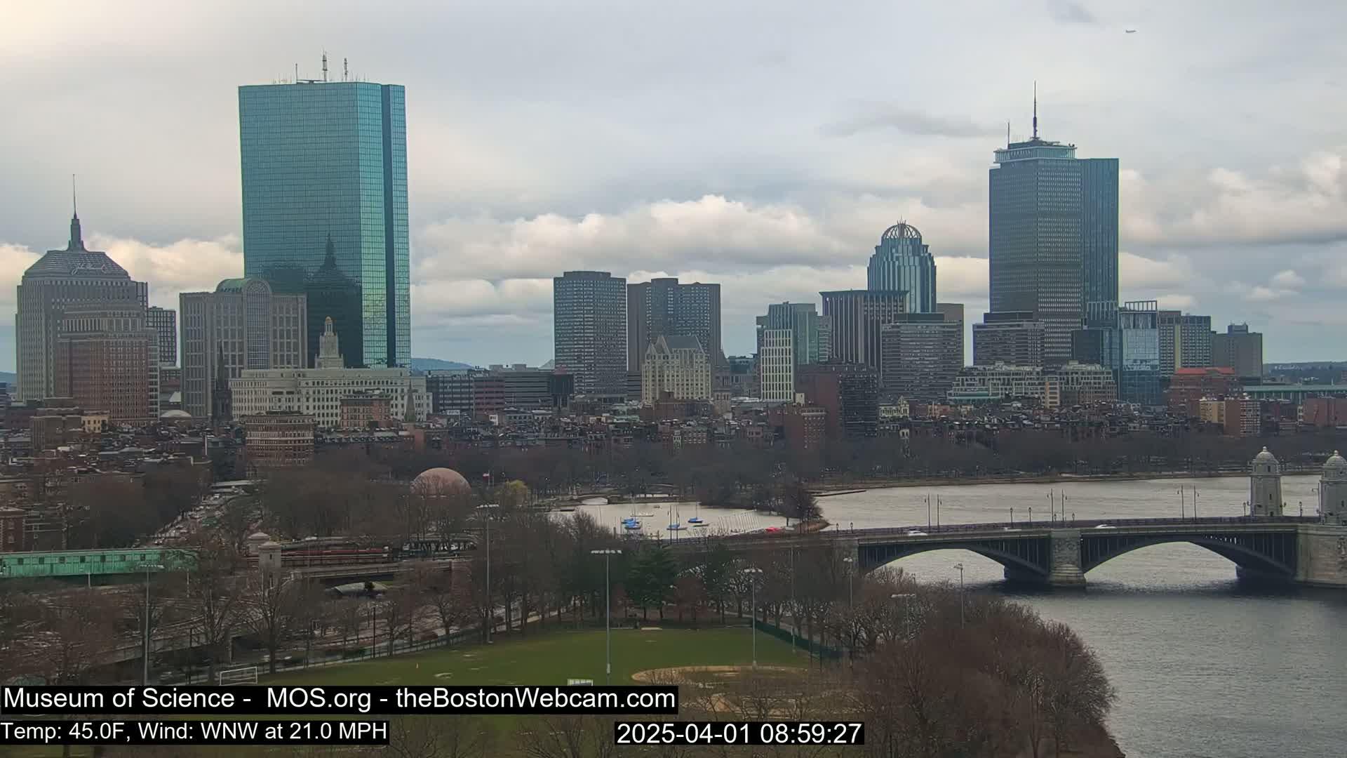 A cityscape with numerous skyscrapers and a bridge spans a river under a cloudy sky.