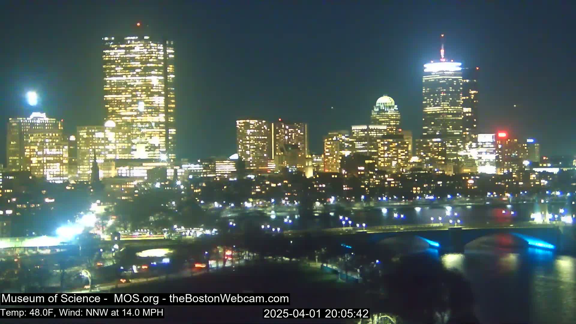 A nighttime view of a city skyline with numerous illuminated buildings across a river, under a clear sky.