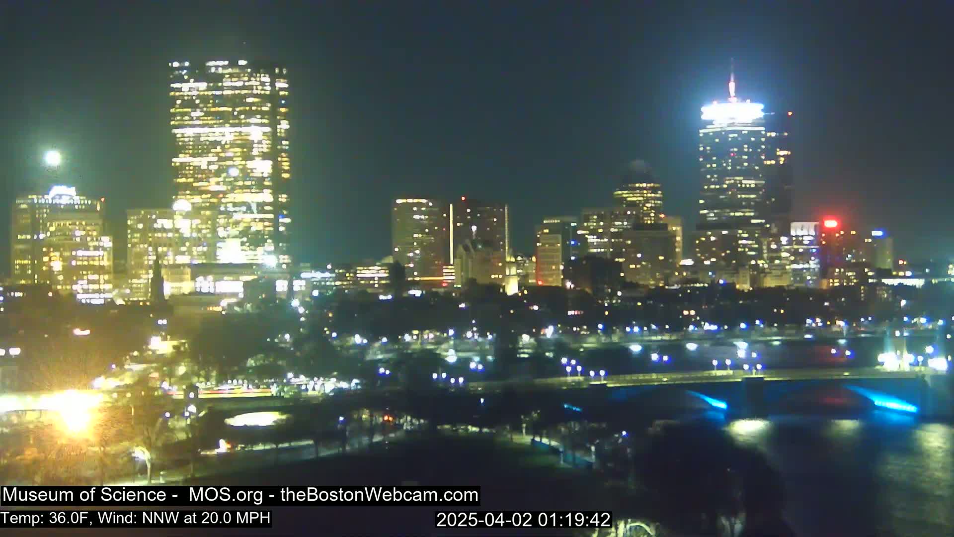 A nighttime cityscape with illuminated skyscrapers and bridges, under a clear sky with a NNW wind at 20 mph and a temperature of 36°F.
