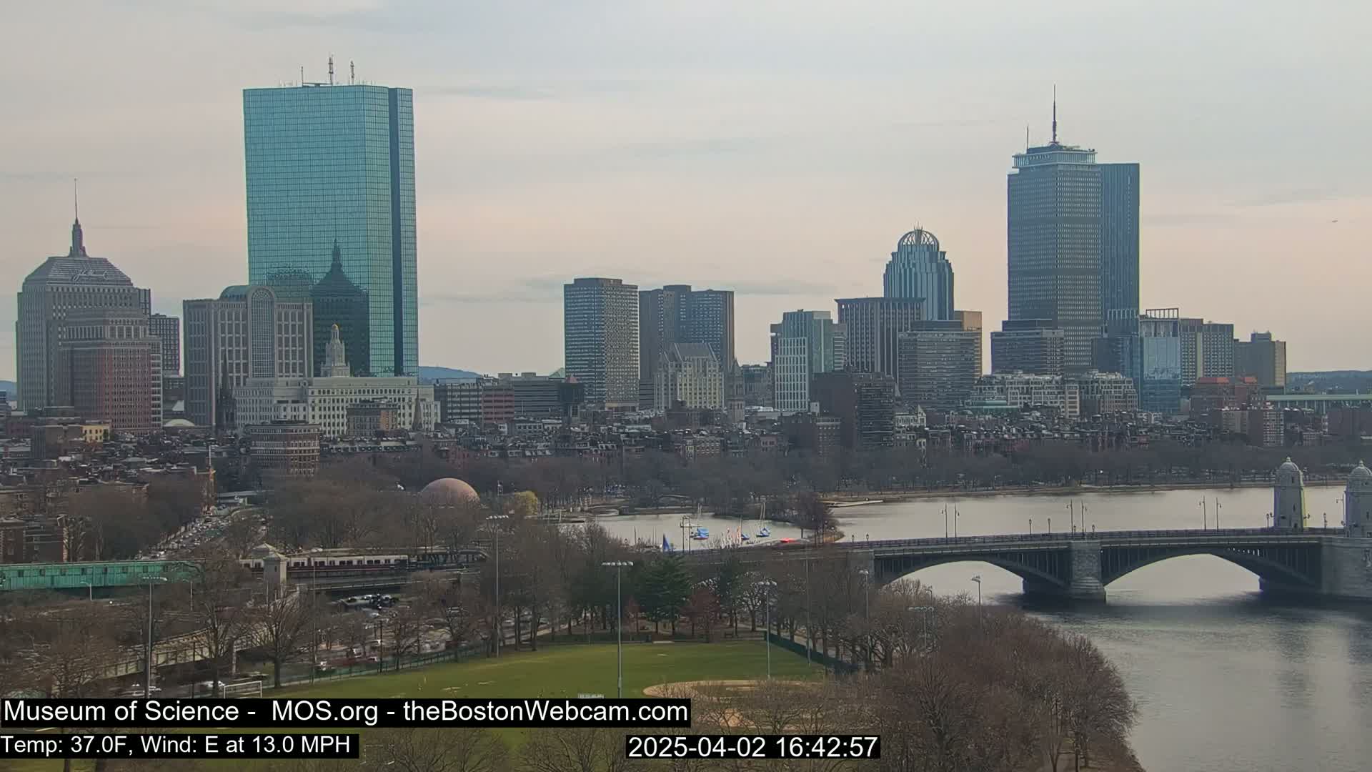 A cityscape with numerous skyscrapers is shown on a partly cloudy day, with a bridge spanning a river in the foreground.