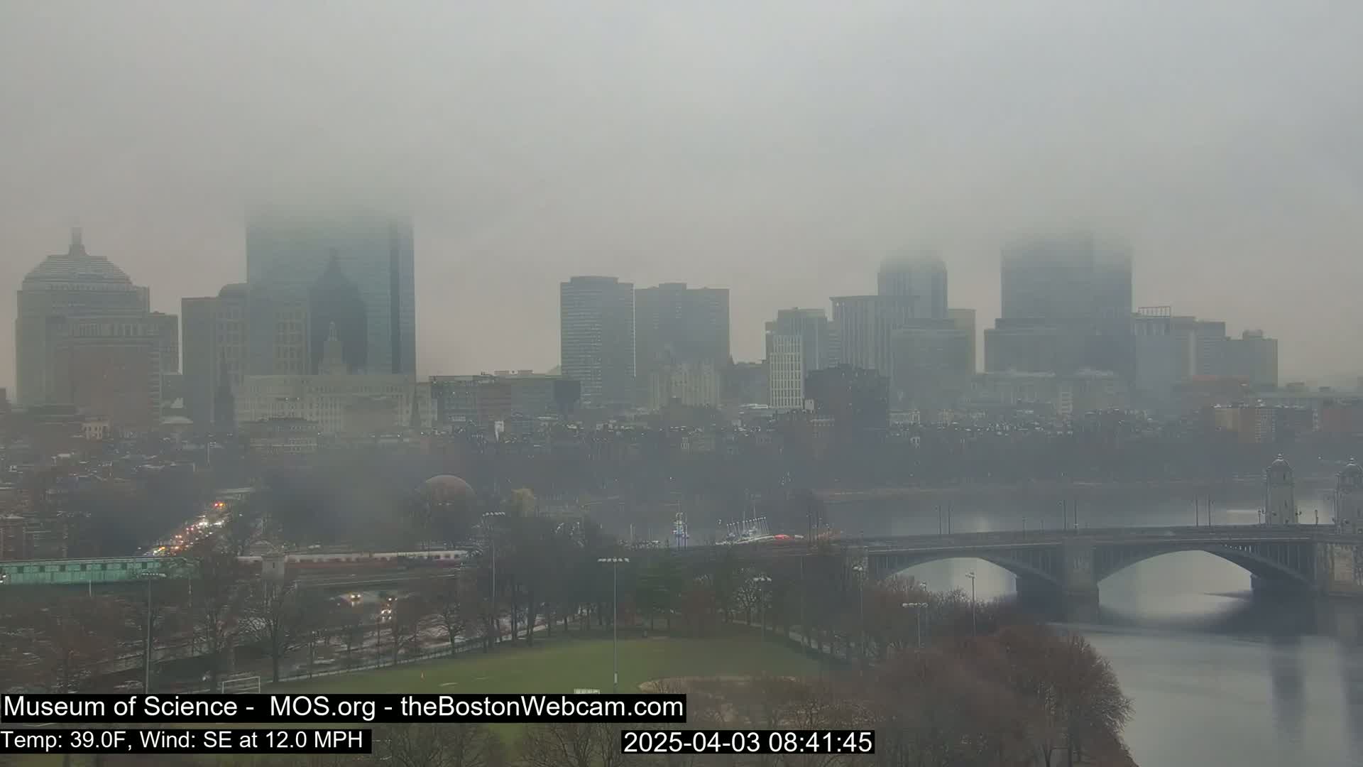 A foggy cityscape with a bridge over a river is visible, and trees line the waterfront.
