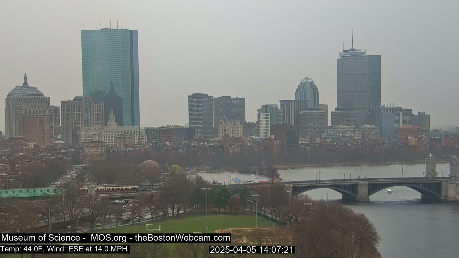 A hazy view of the Boston skyline, including several skyscrapers and a river with a bridge, on a cool, overcast day with a wind from the east-southeast.