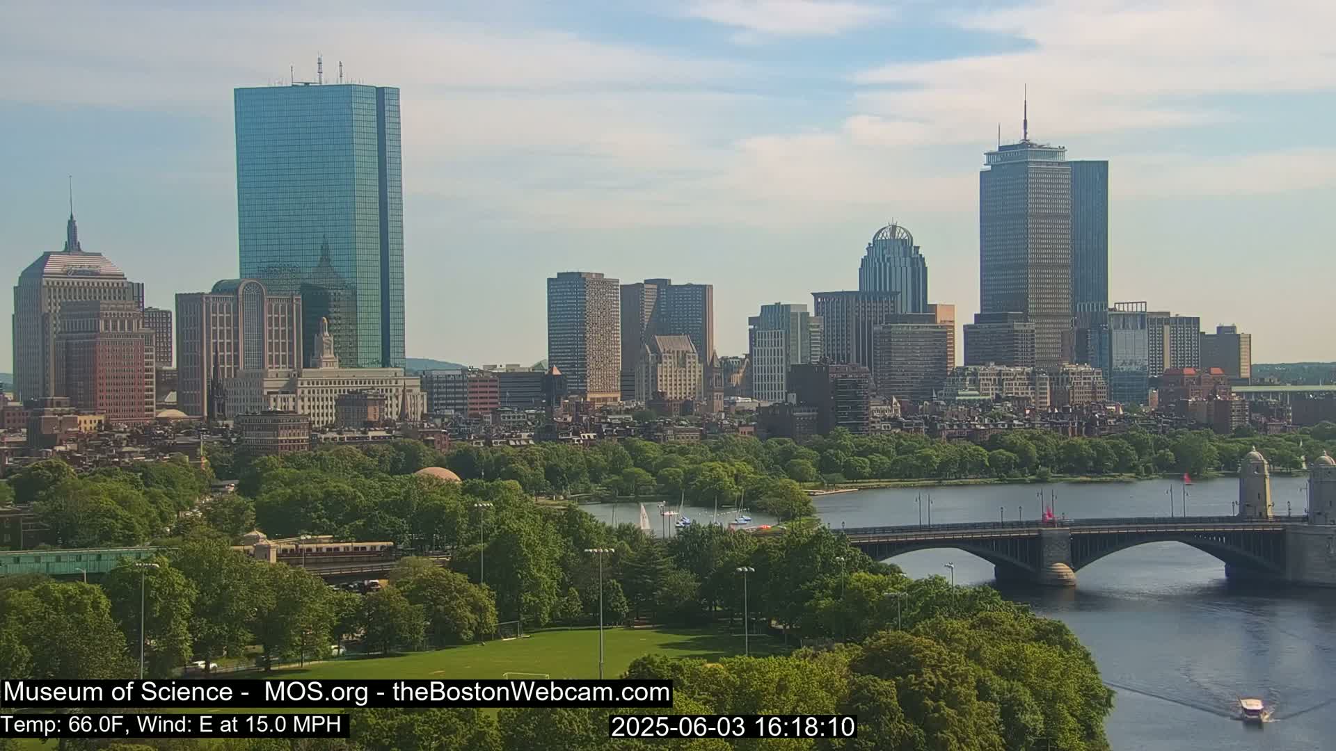 A cityscape with numerous skyscrapers is visible across a body of water with a bridge, under partly cloudy skies.