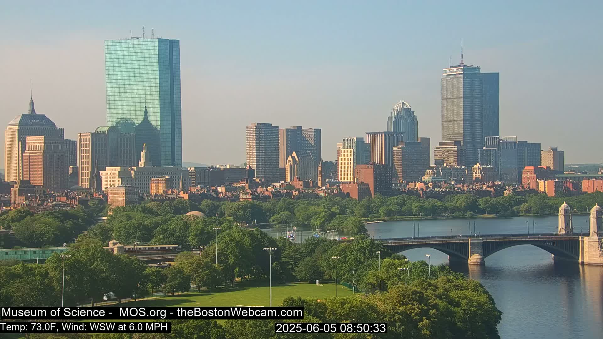 A city skyline with numerous skyscrapers and a bridge over a river, on a clear, sunny day with a light wind.