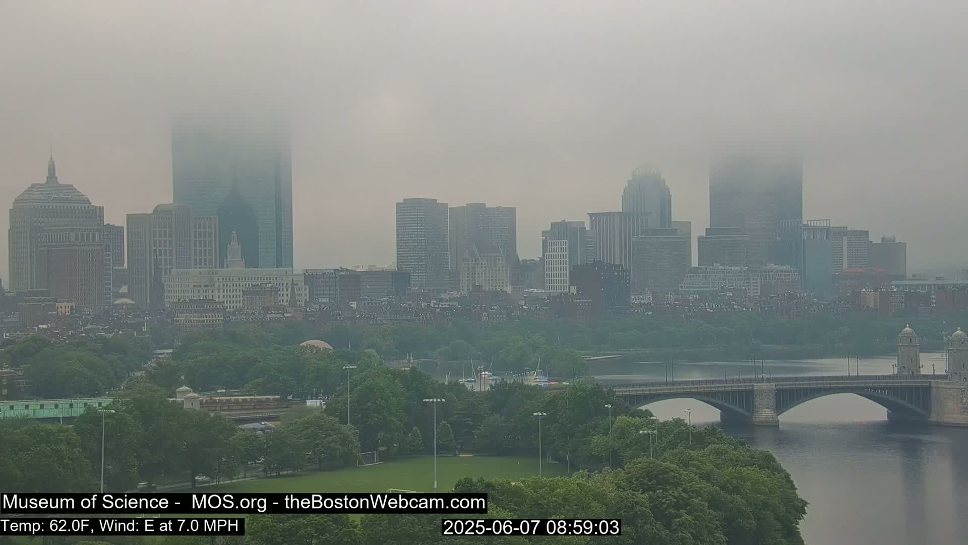 A foggy cityscape with skyscrapers and a bridge over a river.