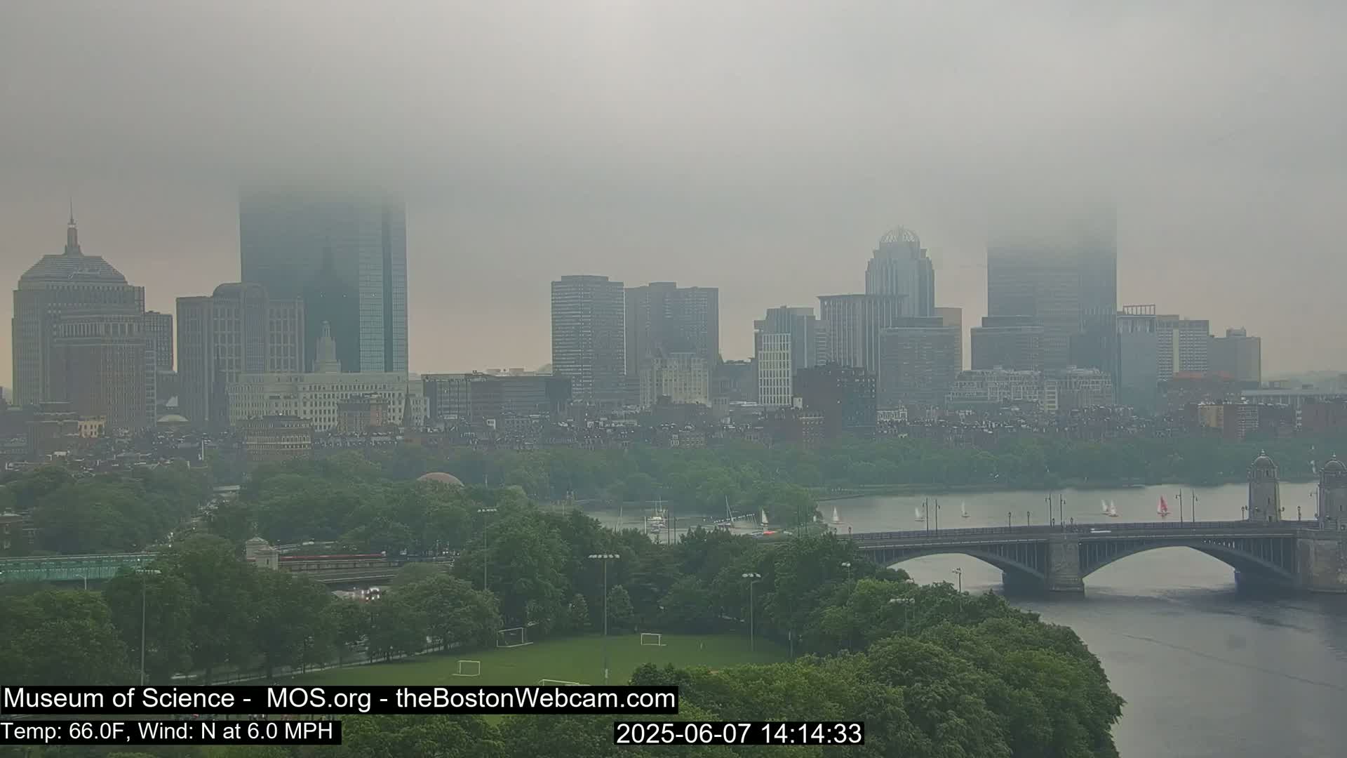 A foggy cityscape with a river and bridge is visible, with several sailboats on the water.