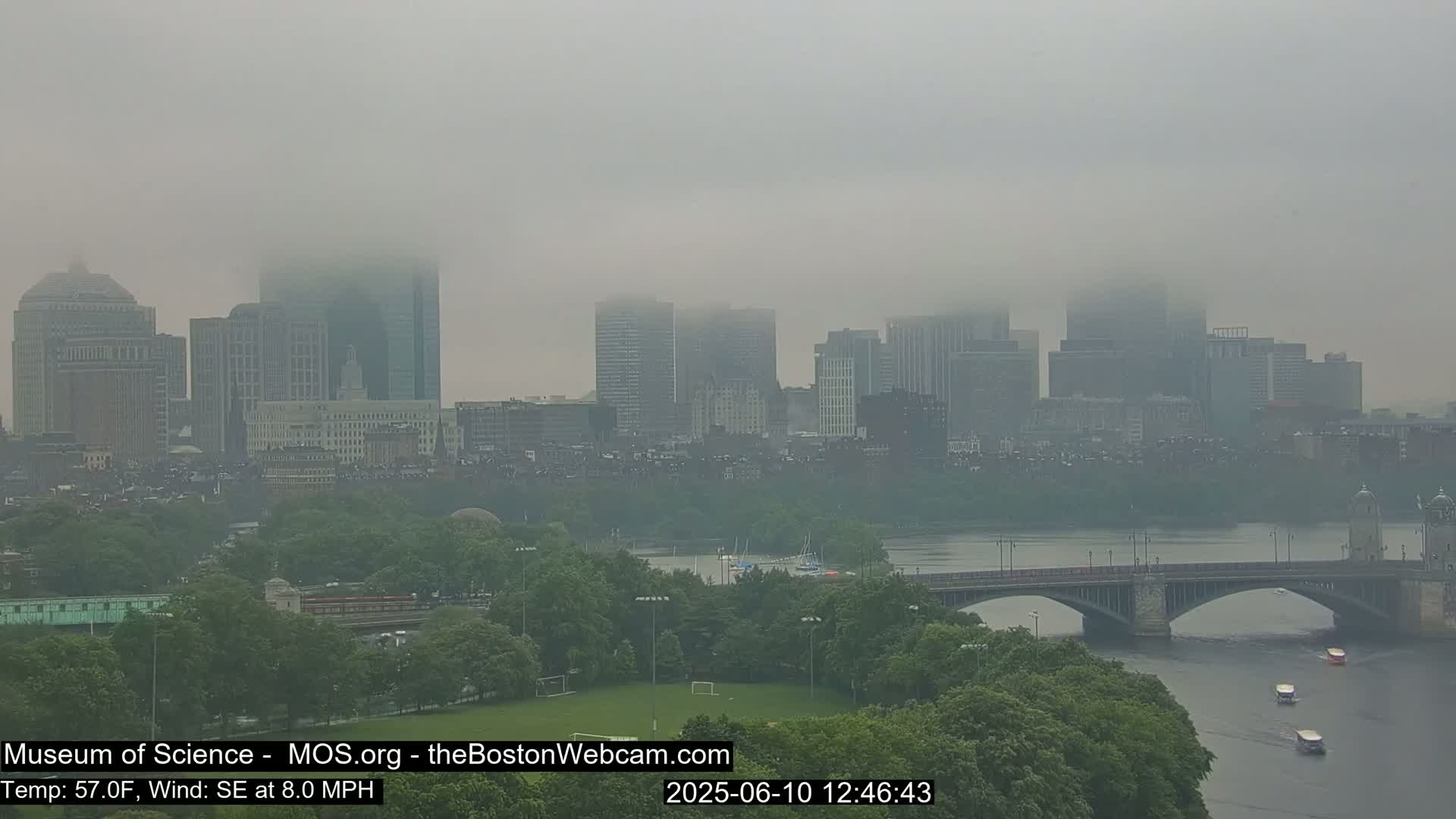 A foggy cityscape with a river and bridge is visible, with several boats on the water.