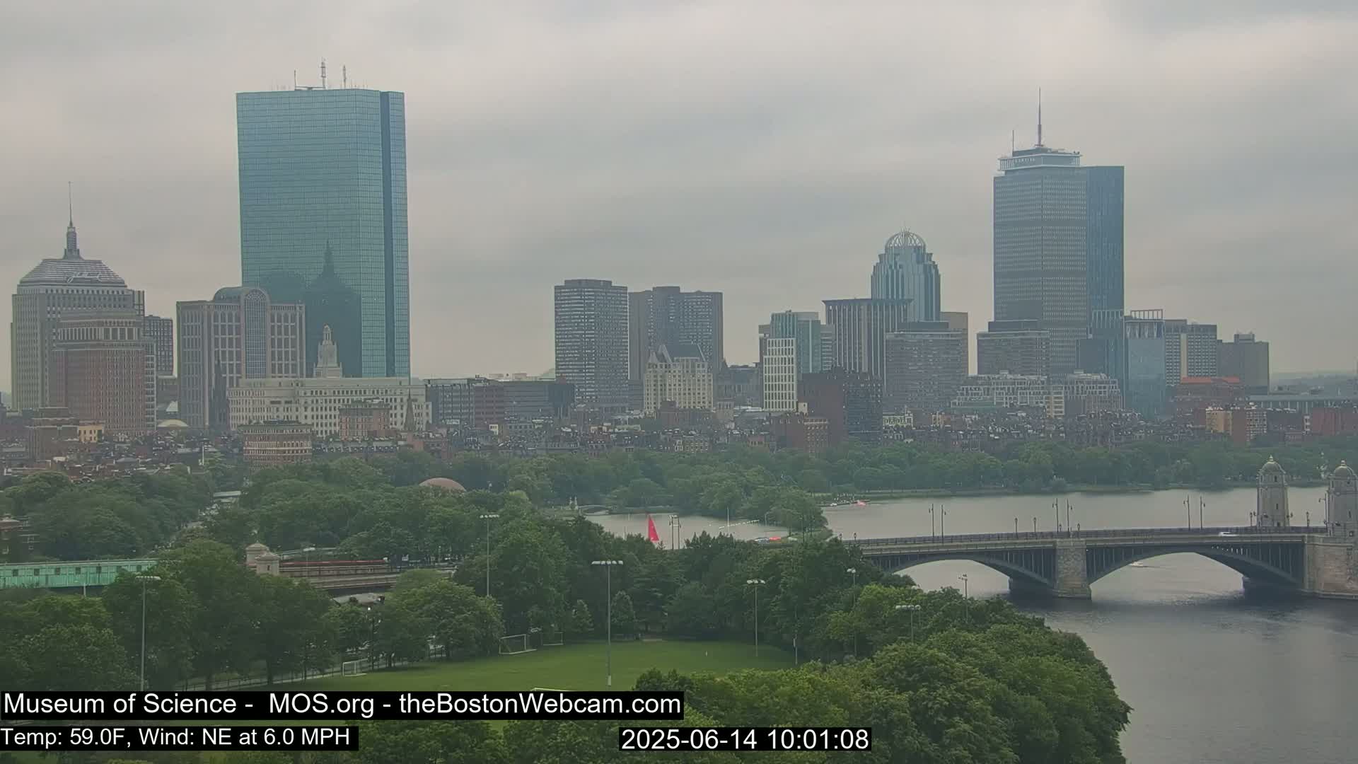 A hazy cityscape with several skyscrapers and a bridge over a river, under an overcast sky.