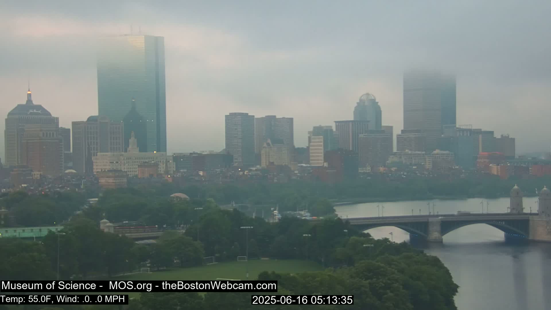 A hazy, foggy view of a city skyline across a river, with a bridge in the foreground.