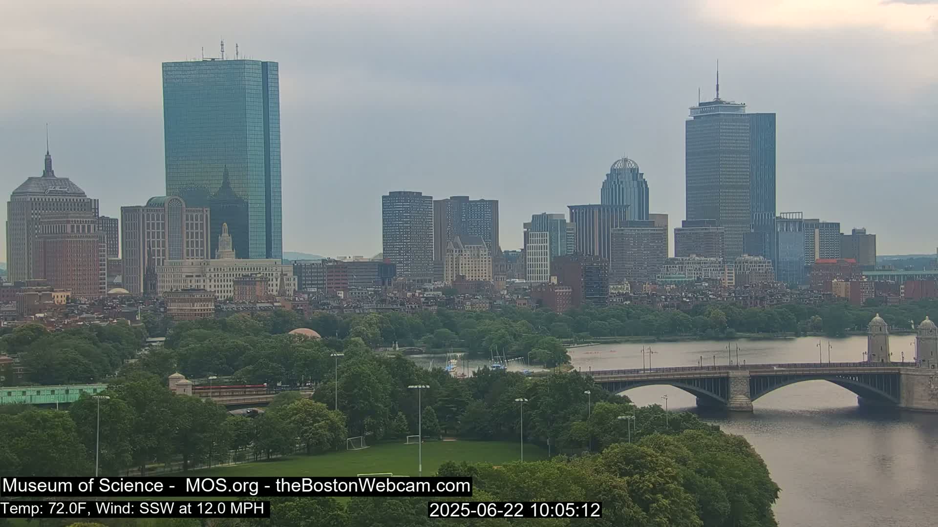 A cityscape with numerous skyscrapers and a bridge over a river, under overcast skies.