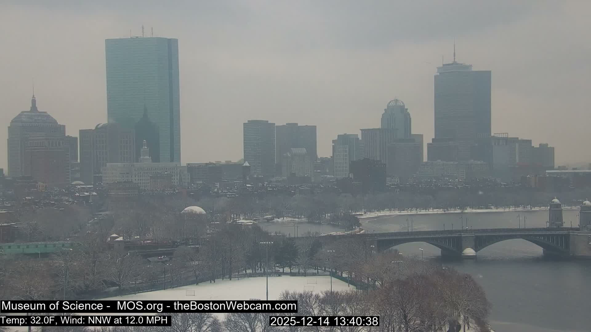 A sprawling city skyline glows brightly at night with countless lights from buildings, reflected on a body of water, under a clear, dark sky.