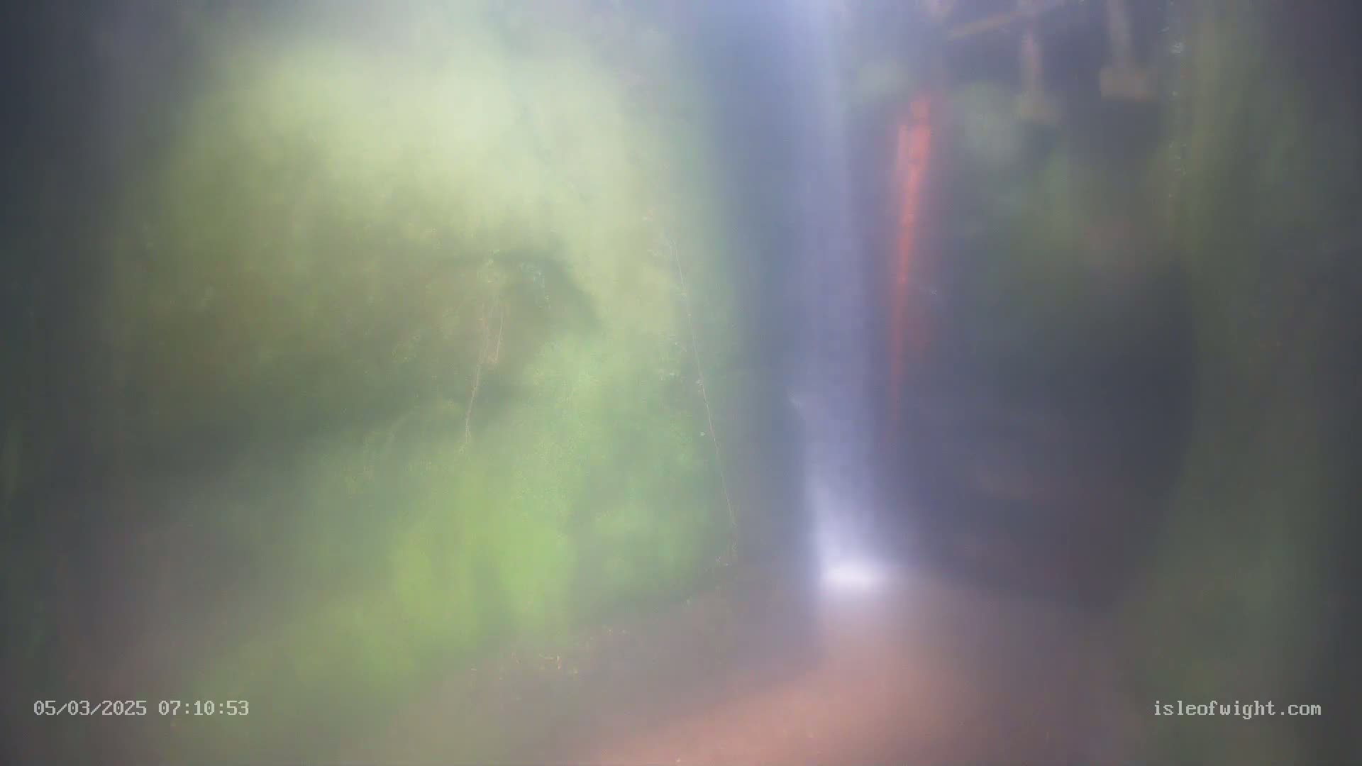 A blurry, misty view shows a waterfall cascading down mossy, green rocks.