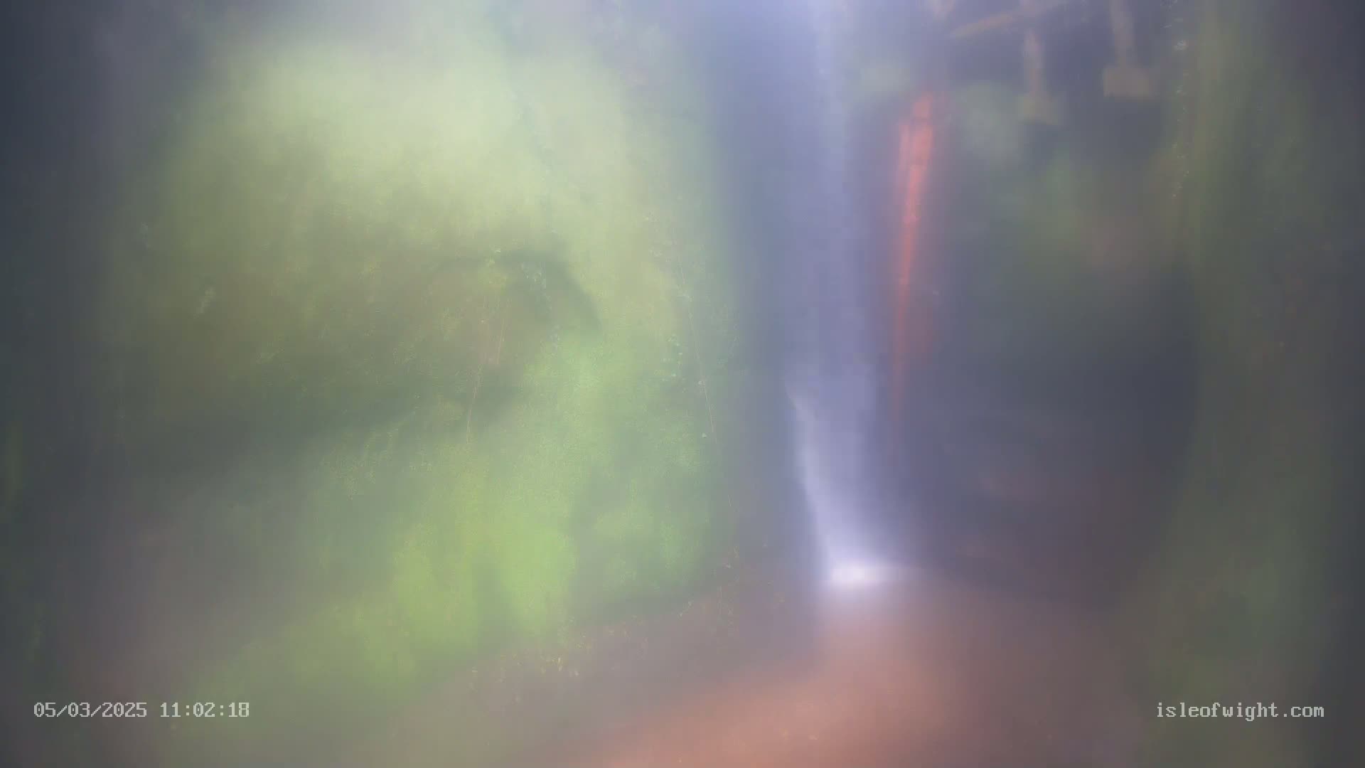 A hazy view of a waterfall cascading through mossy, green rock formations.
