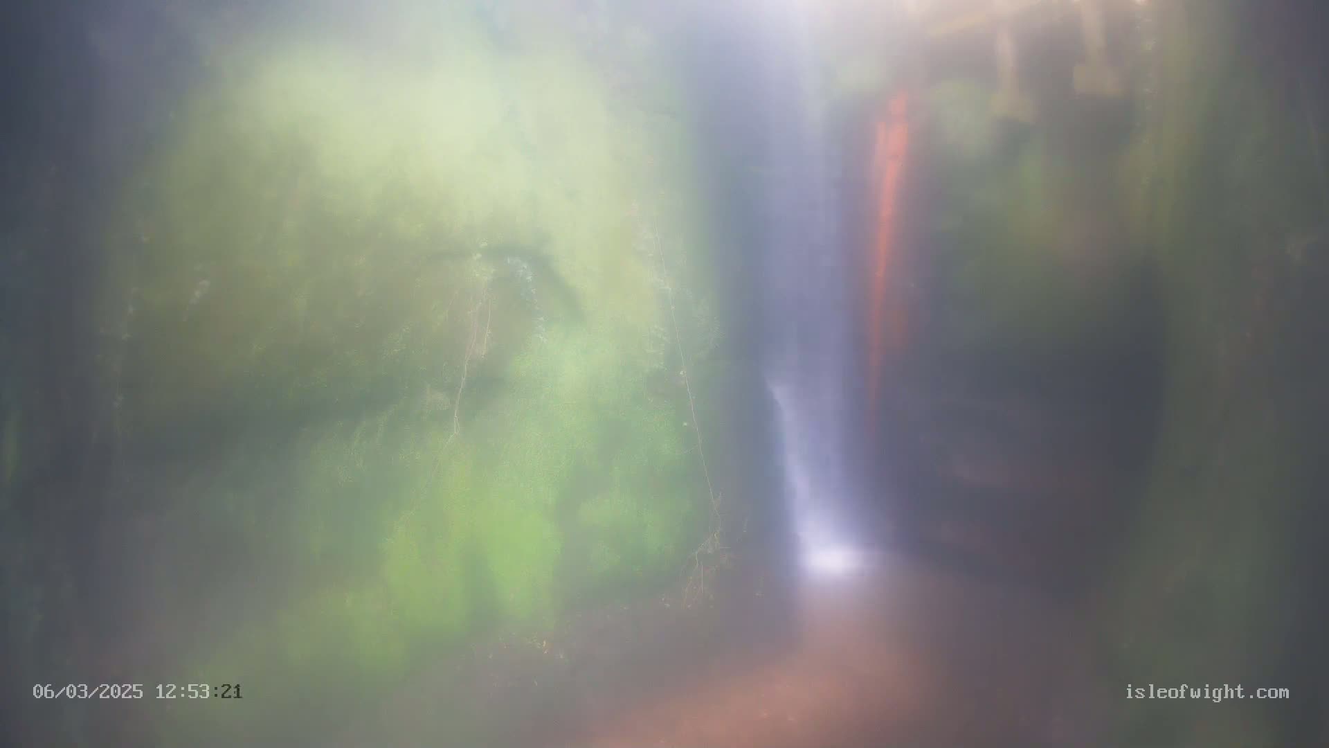 A misty waterfall flows between moss-covered rocks.