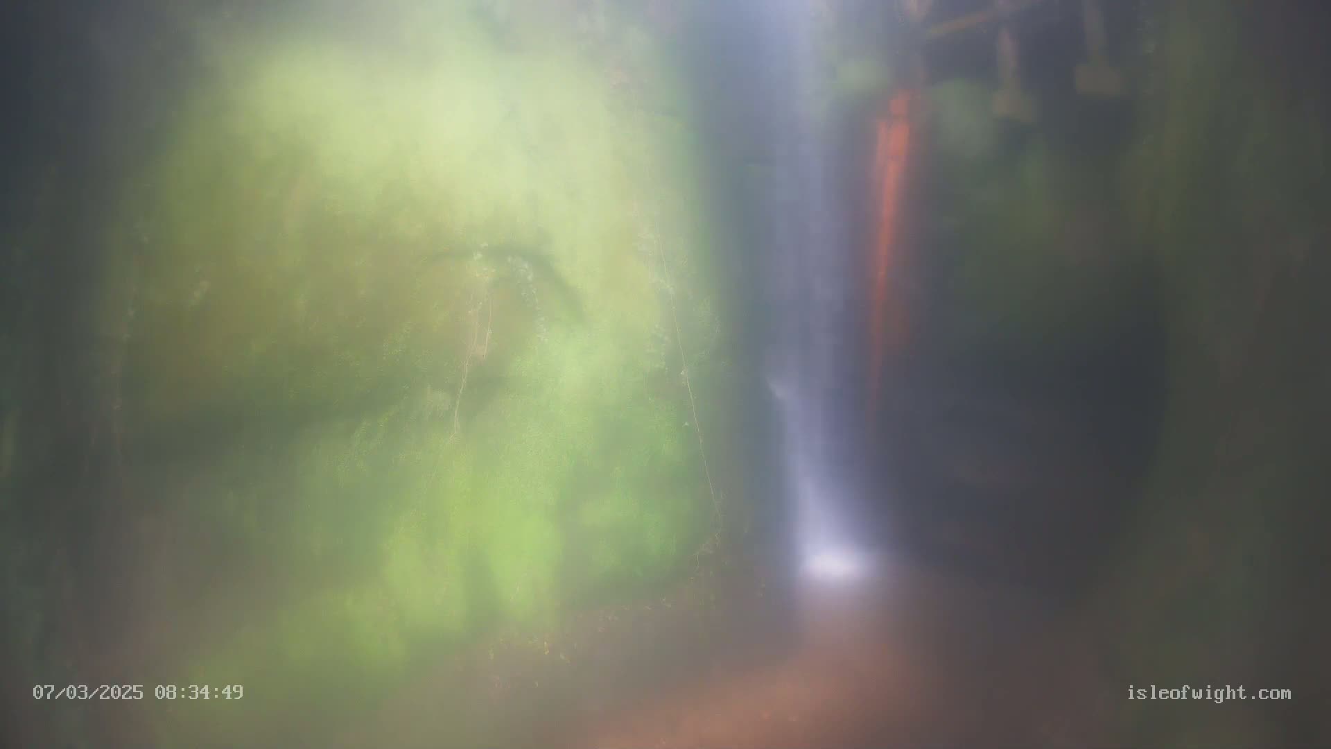 A blurry image shows a waterfall cascading down mossy rocks in misty conditions.