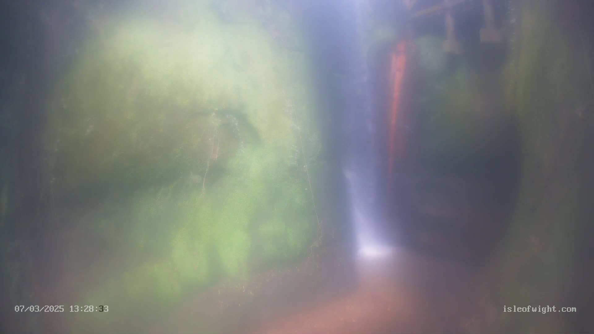 An underwater view shows a hazy, light-filled space between mossy, green rock formations.