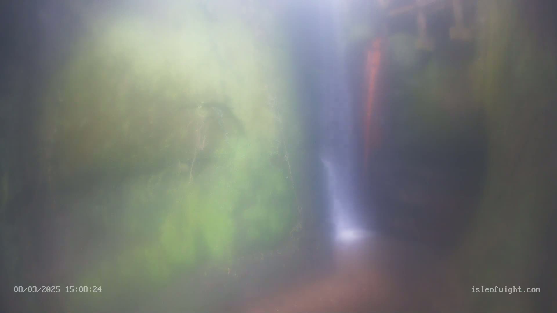 A blurry image shows a waterfall partially obscured by mist and lush green foliage.