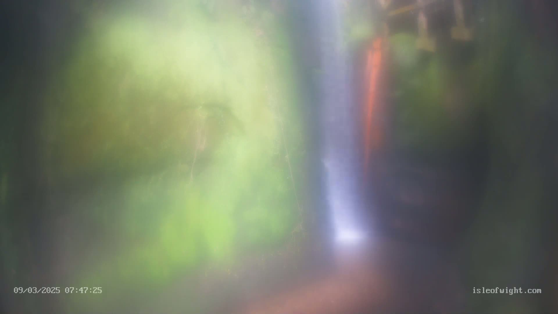 A blurry image shows a waterfall partially obscured by mist and lush green foliage.