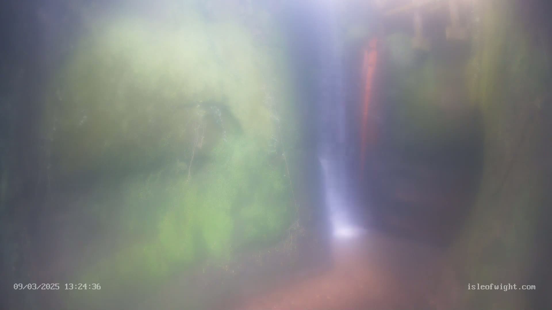 A blurry image shows a narrow waterfall cascading down mossy rock faces in misty conditions.