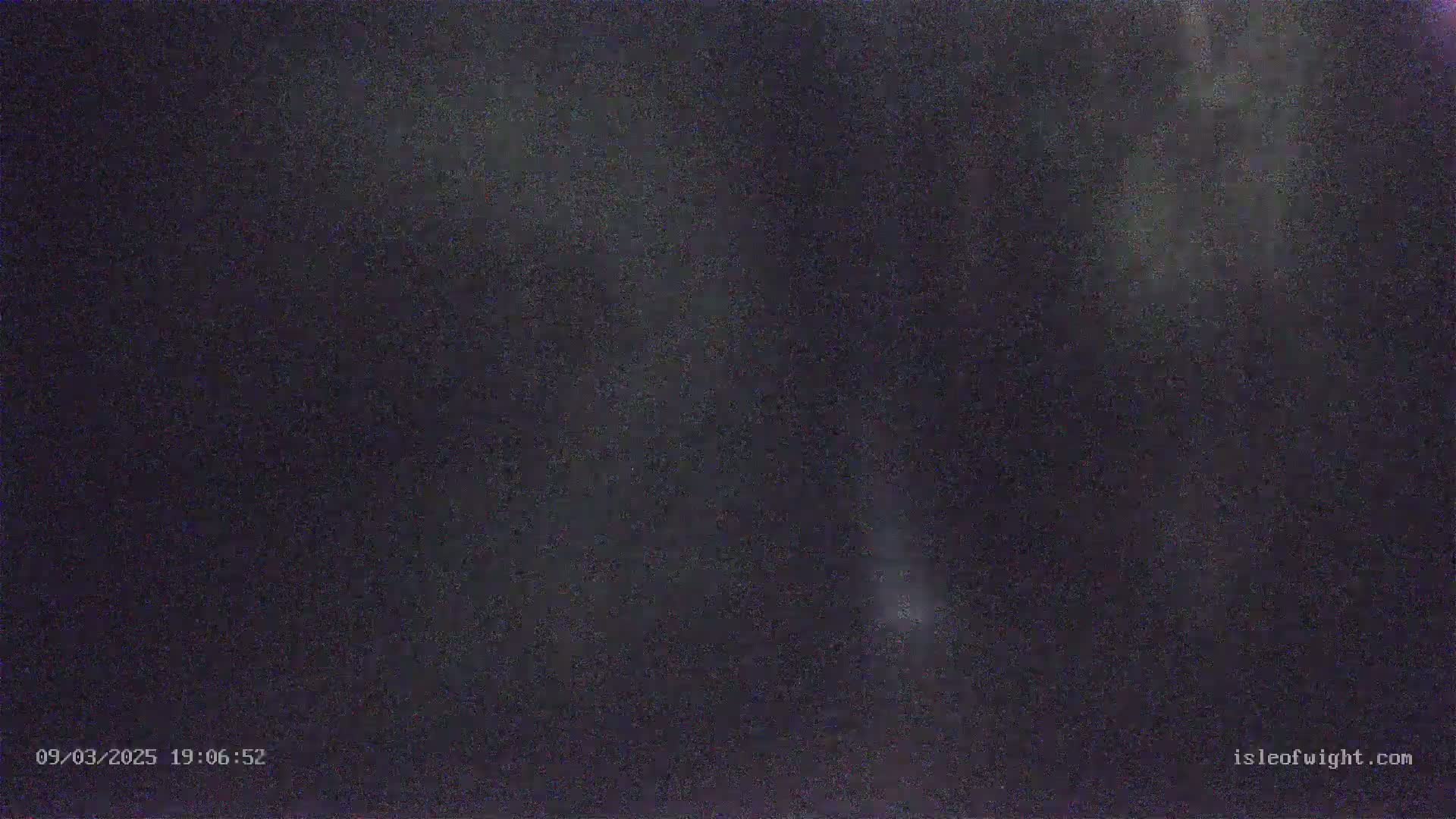 A nighttime, dark image shows a grainy, blurry view with a lighter vertical streak in the center.