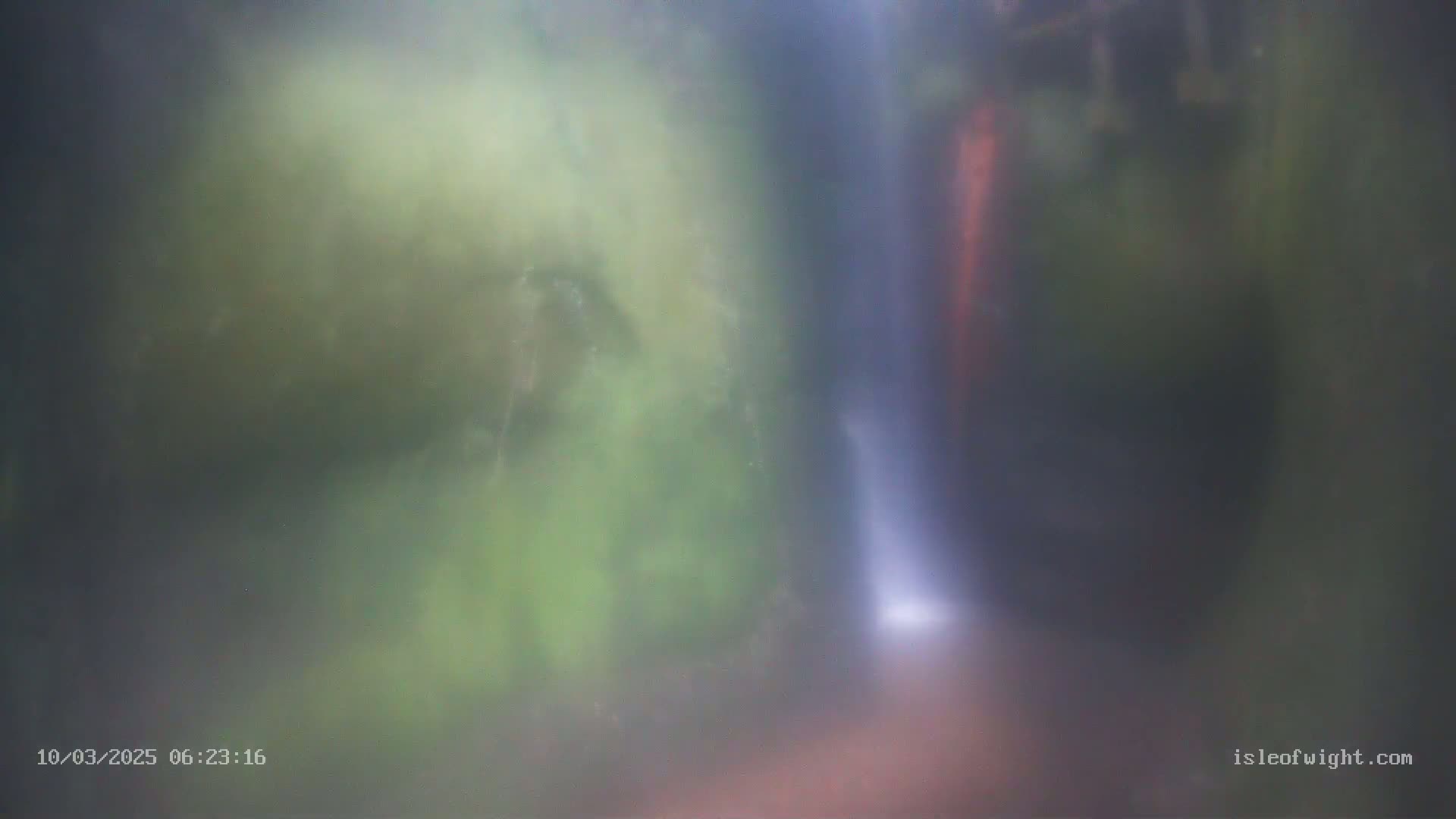 A blurry image shows a thin waterfall cascading down a rocky, moss-covered area in misty conditions.