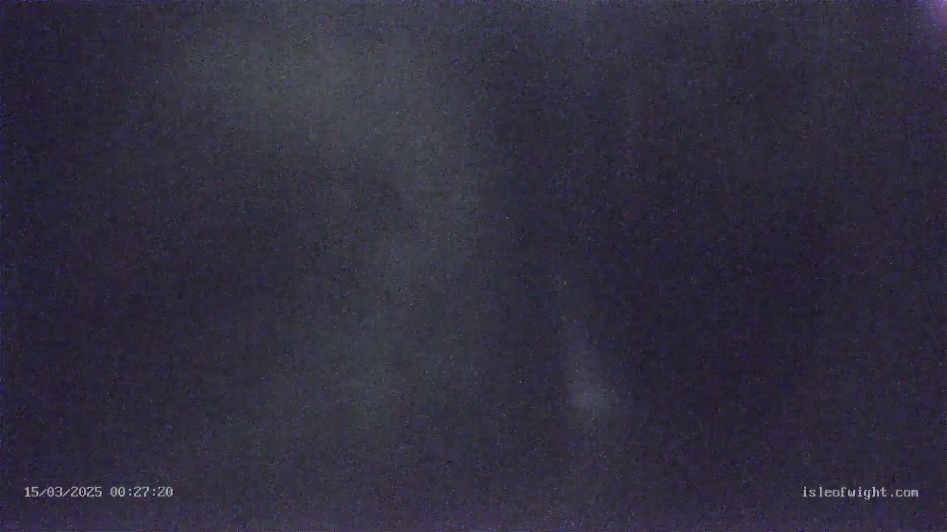 A dark, blurry nighttime image shows a mostly clear sky with some faint light sources.