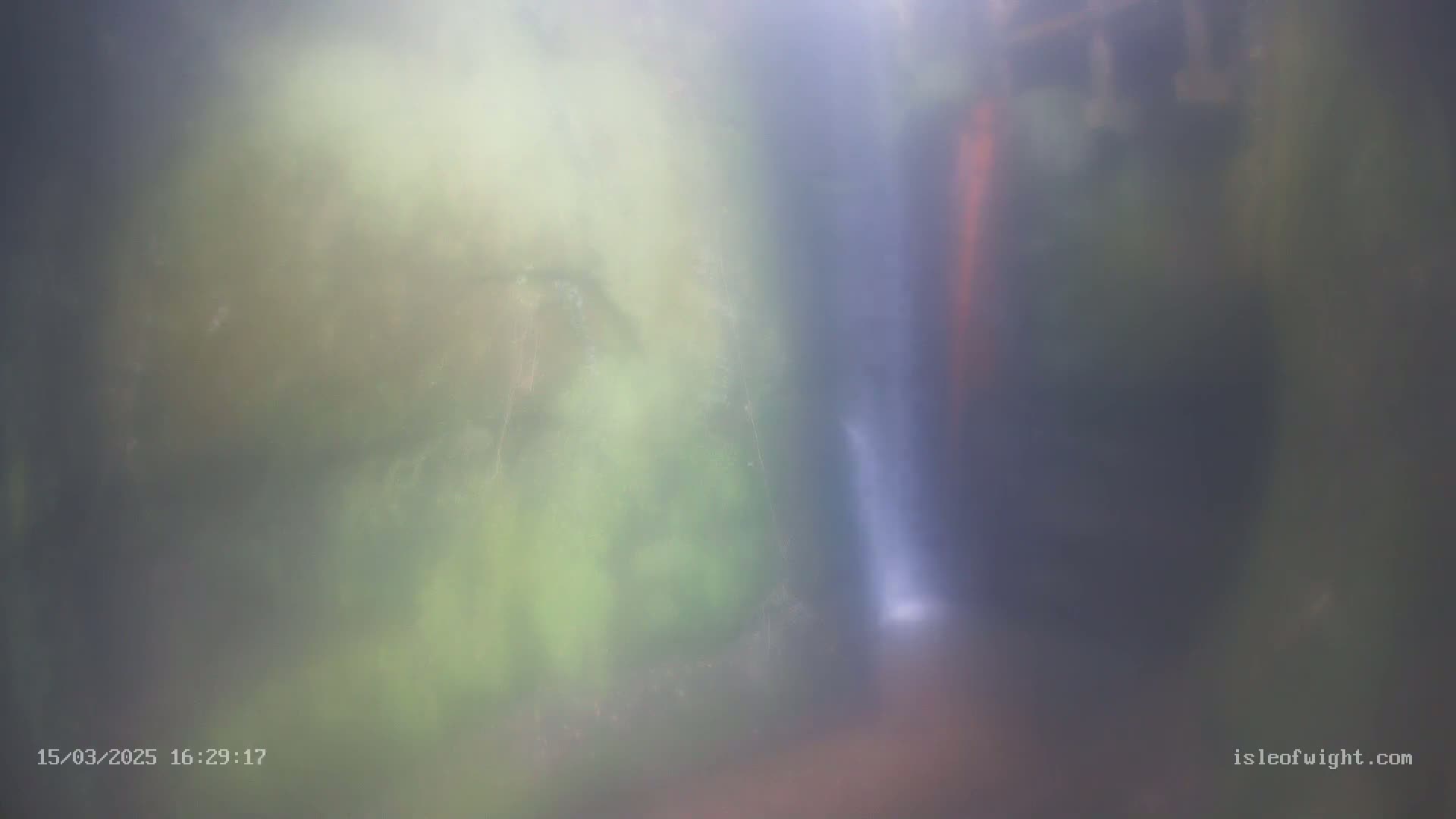 A blurry image shows a waterfall partially obscured by mist in a lush green forest.