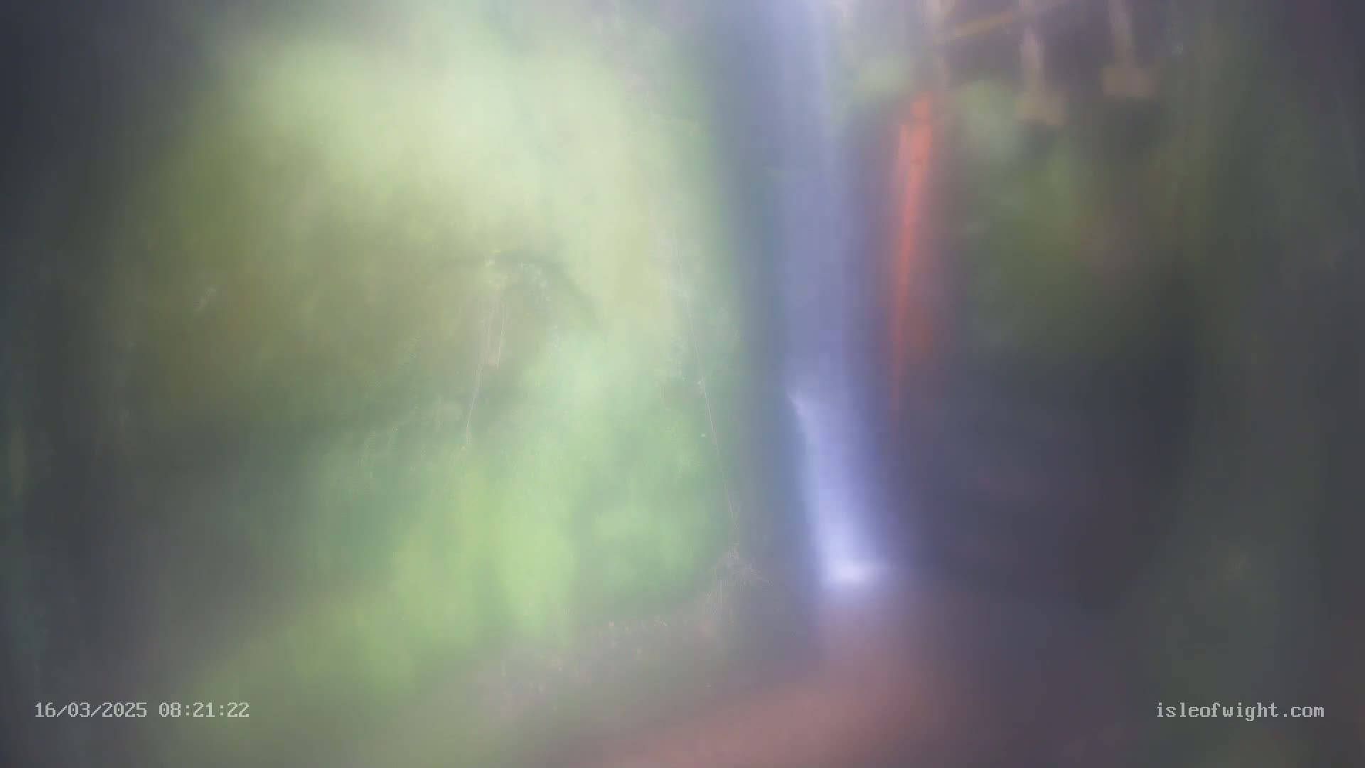 A blurry image shows a thin waterfall cascading down a rock face partially obscured by mist and vegetation.
