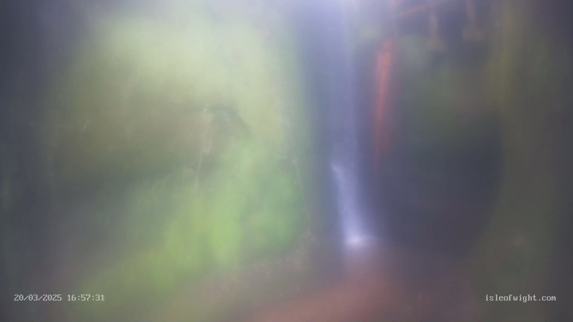 A blurry image shows a misty waterfall cascading down a rock face surrounded by green vegetation.