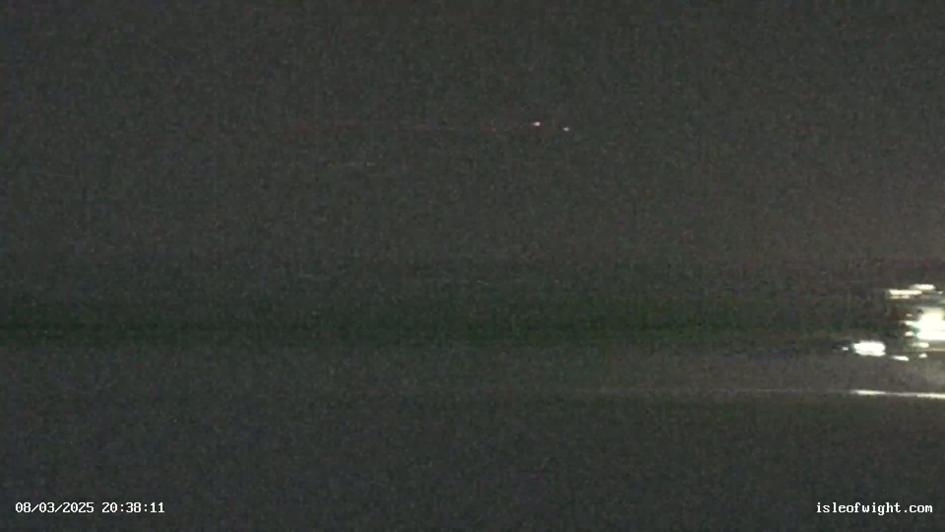 A nighttime view of a dark, flat expanse, possibly water or land, under a clear, dark sky with a few faint lights visible in the distance.