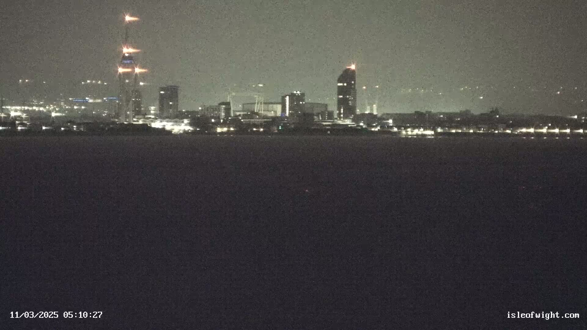 A nighttime view of a city skyline across a dark body of water under a cloudy sky.