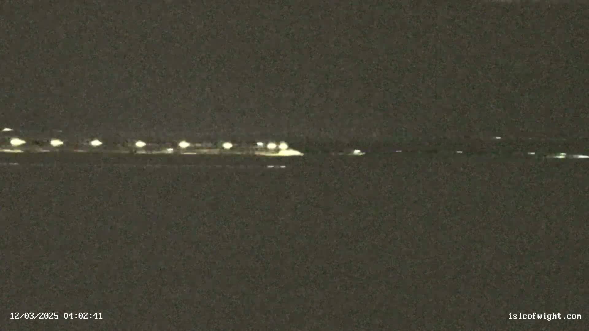A nighttime, low-light view shows a dark body of water with a line of distant lights on the horizon.
