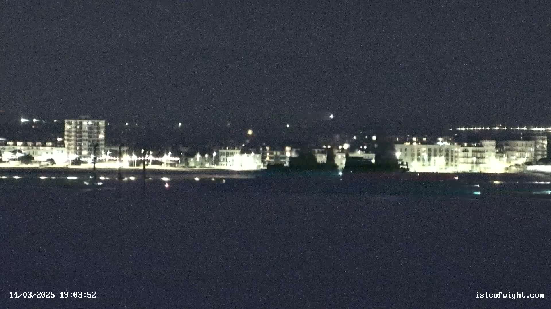 A nighttime view of a city skyline across a dark body of water under a clear, dark sky.