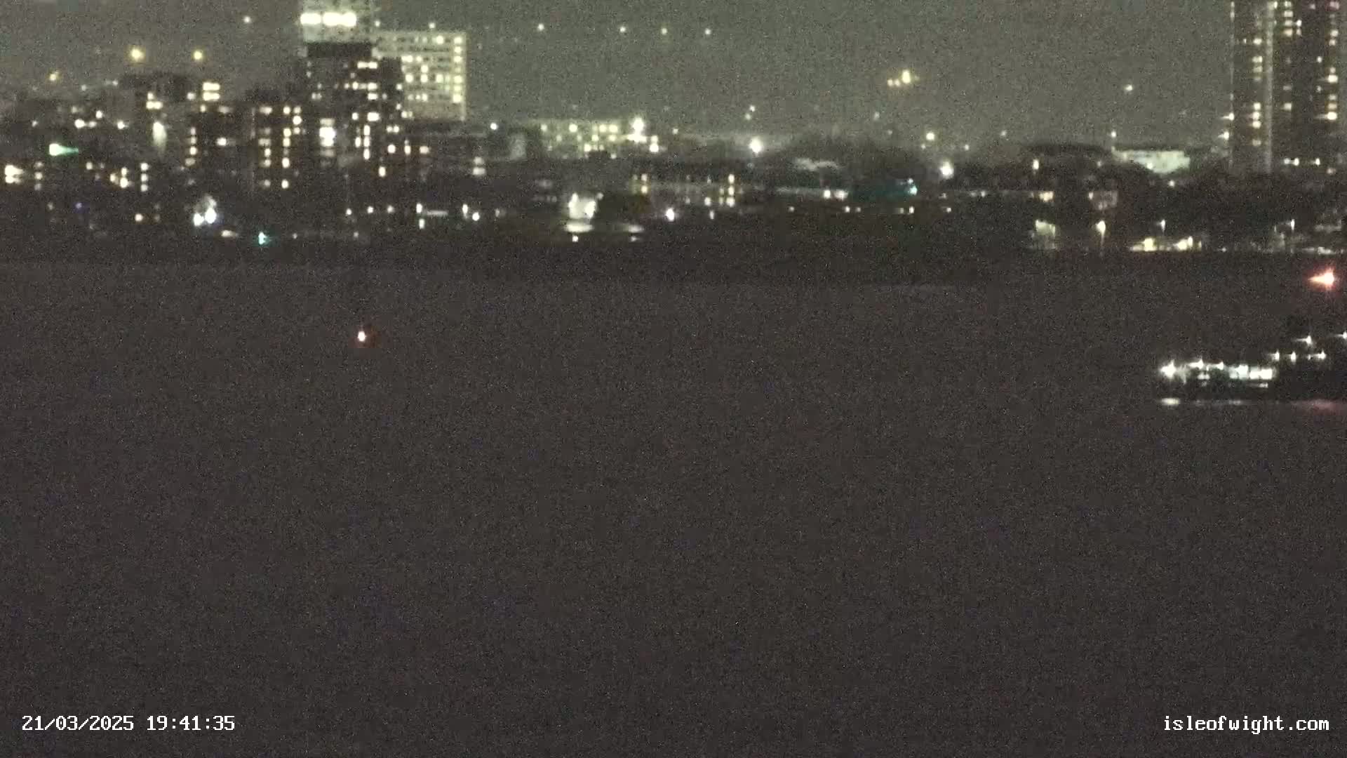 A nighttime view of a city skyline across a dark body of water, under a clear sky.
