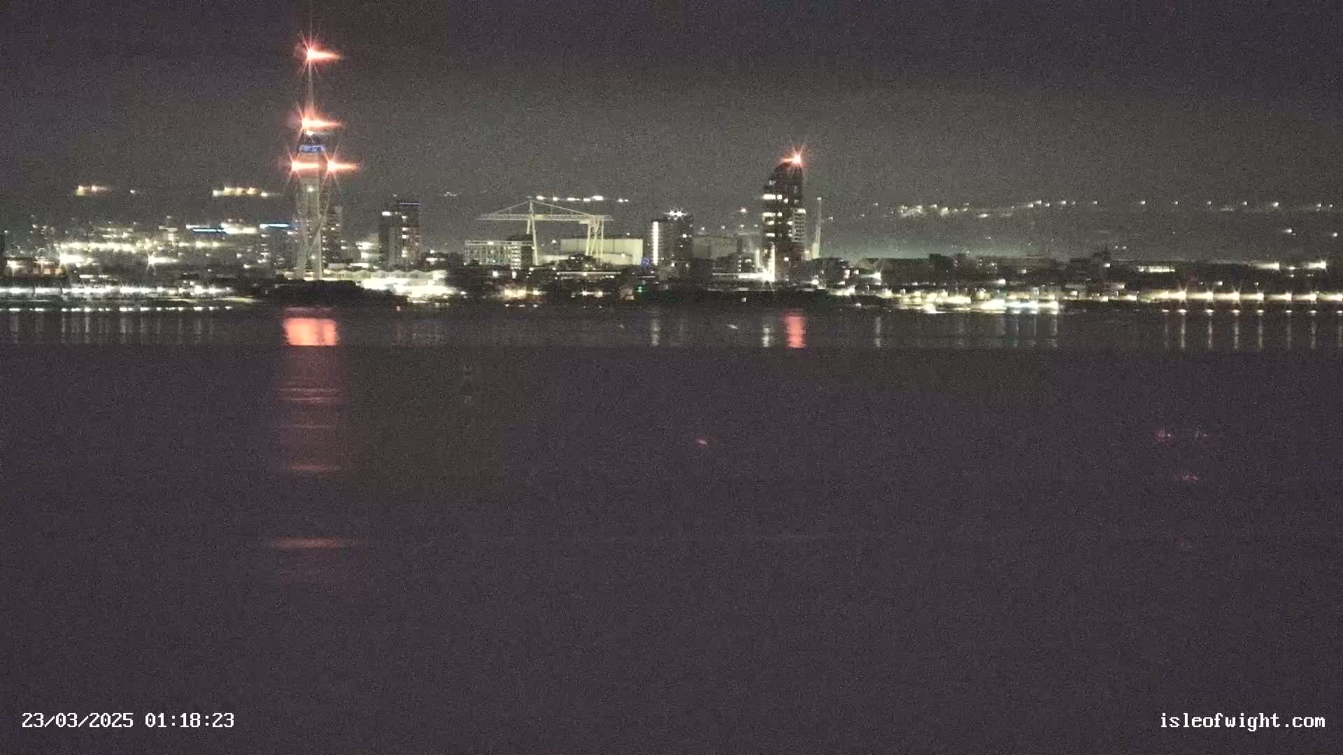 A nighttime view of a city skyline across a body of dark water, reflecting the city lights.