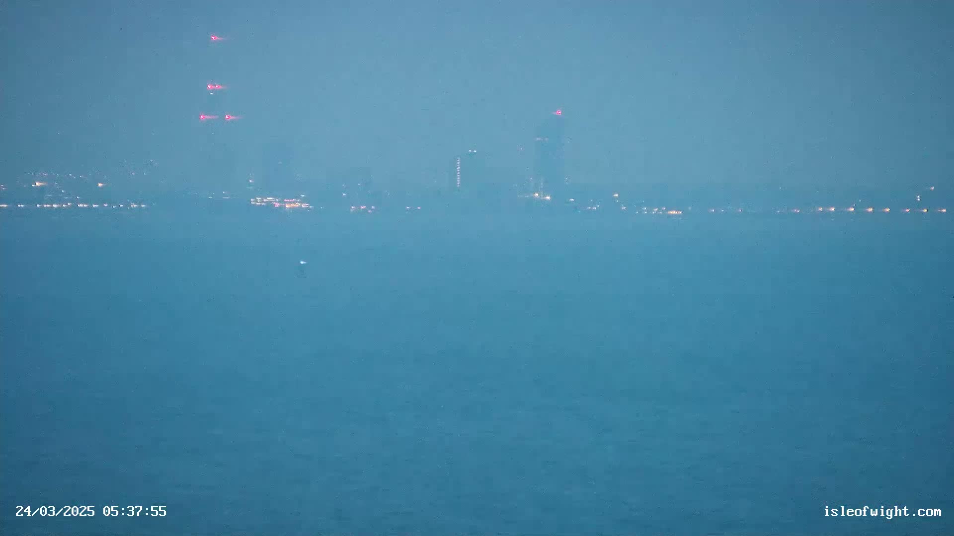 A hazy, dusky view shows a distant city skyline with faint lights across a calm body of water.