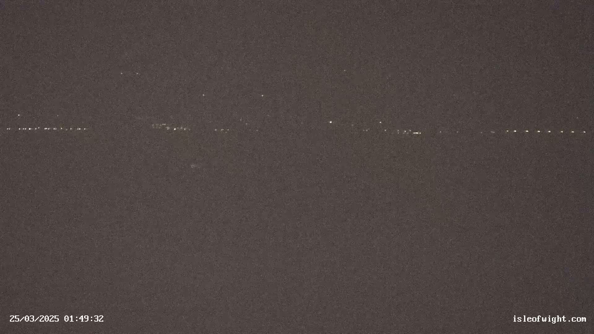 A dark, nighttime image shows a distant line of faint lights across a dark horizon under a clear, dark sky.