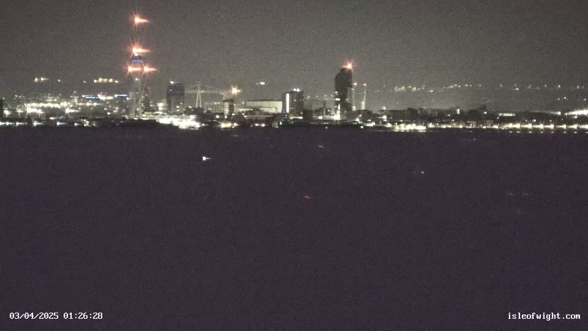 A nighttime view of a city skyline across a dark body of water, under a clear sky.