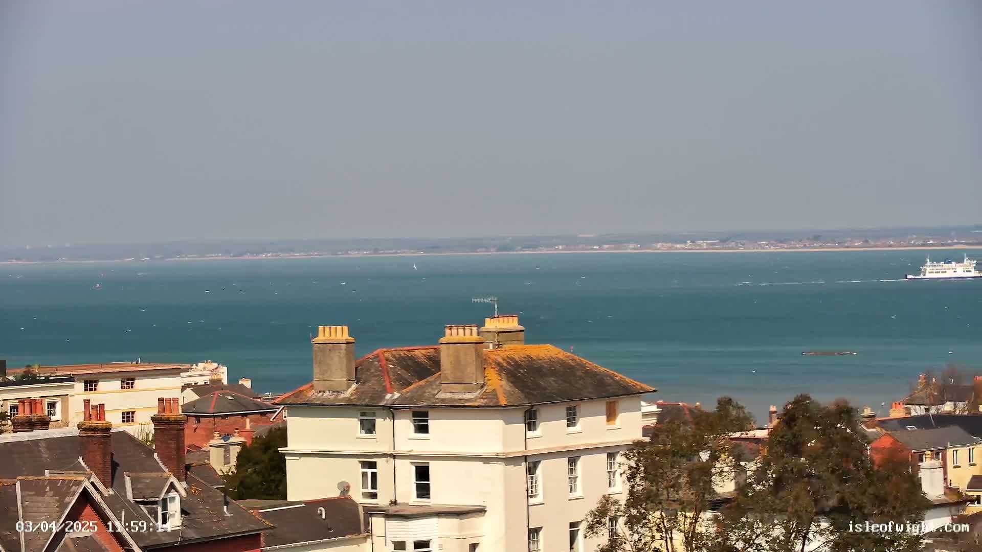 A view of a town with a large body of water and a ferry in the distance on a sunny day.