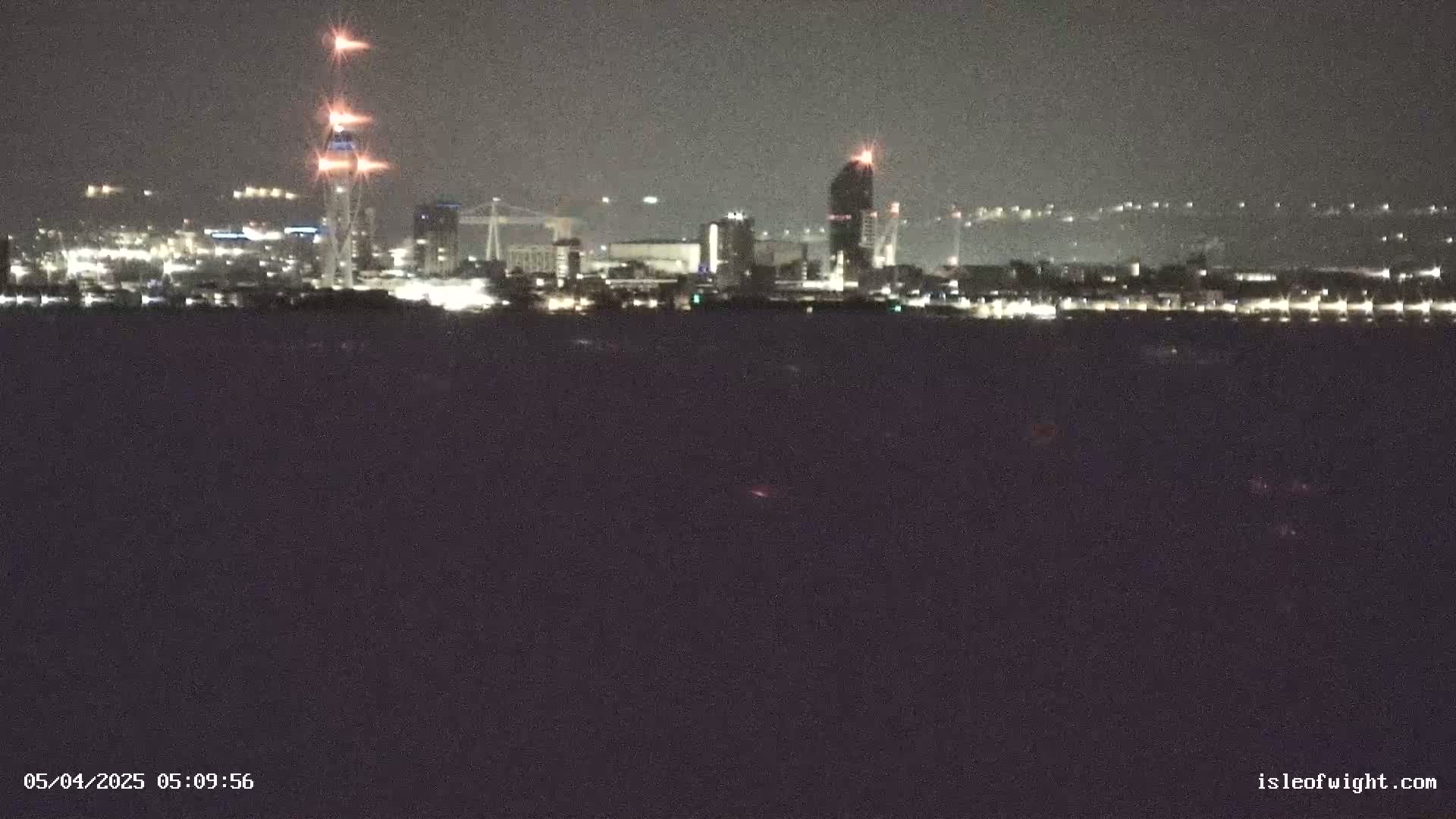 A nighttime view of a city skyline across a dark body of water, with some construction visible.