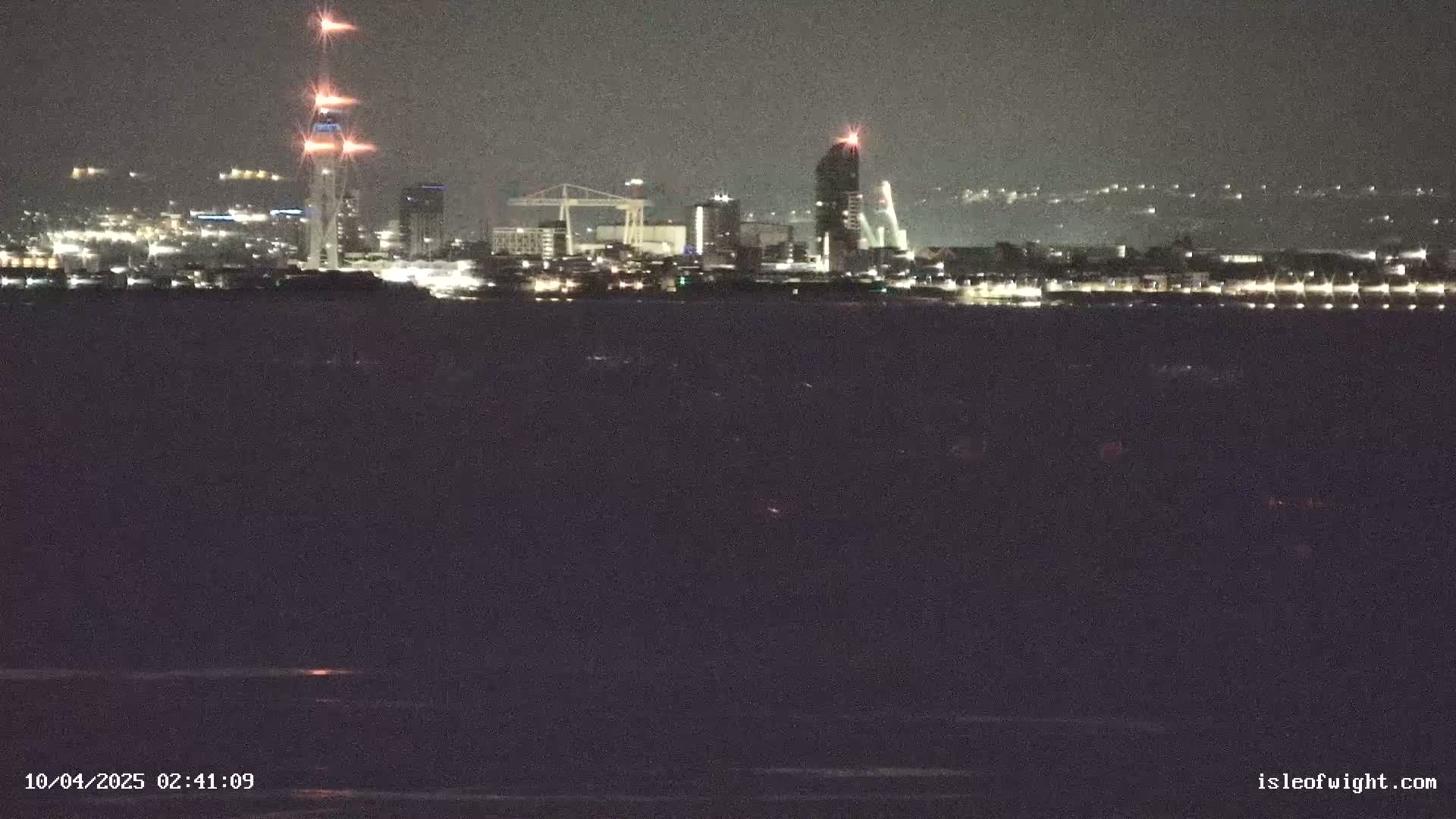 A nighttime view of a city skyline across a dark body of water under a clear sky.