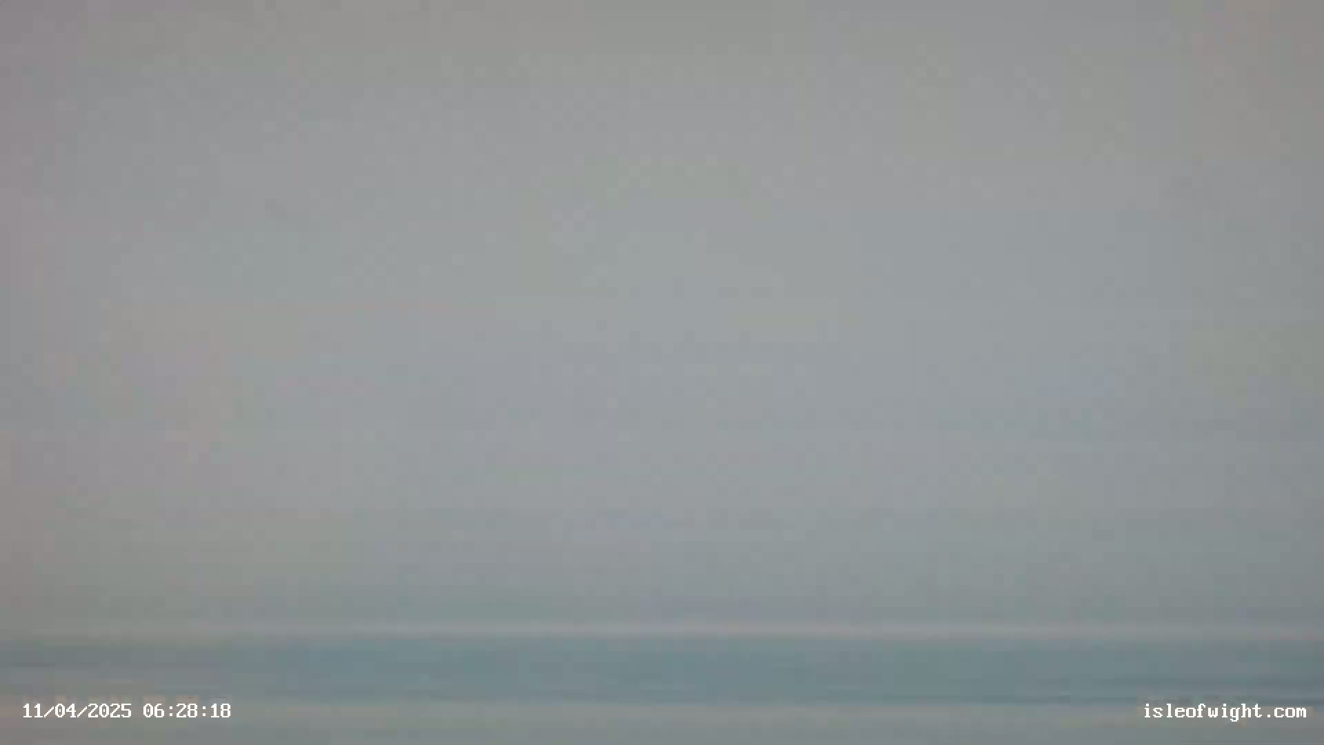 A hazy, overcast sky meets a calm, light-blue body of water at the horizon.
