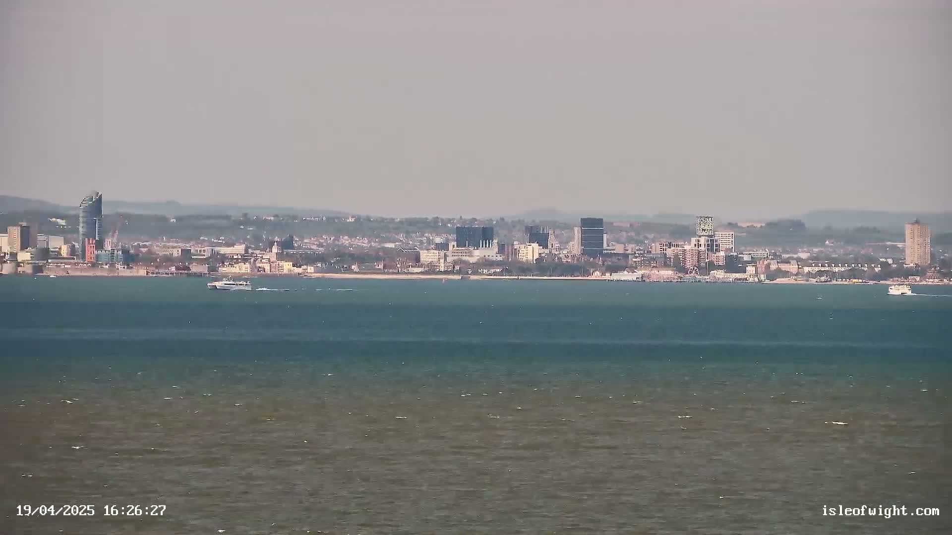 A distant city skyline is visible across a calm body of water on a hazy day.