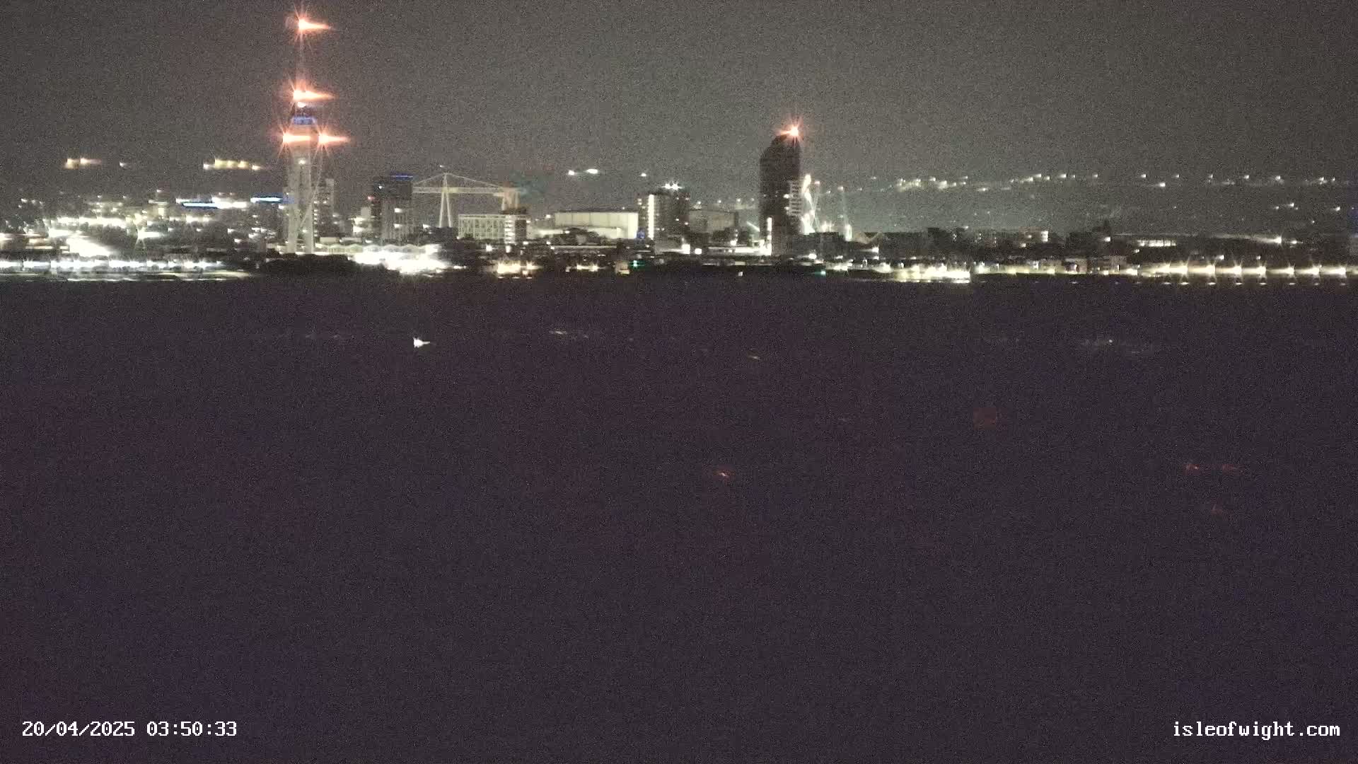 A nighttime view shows a city skyline across a dark body of water, with a tall tower lit up brightly.