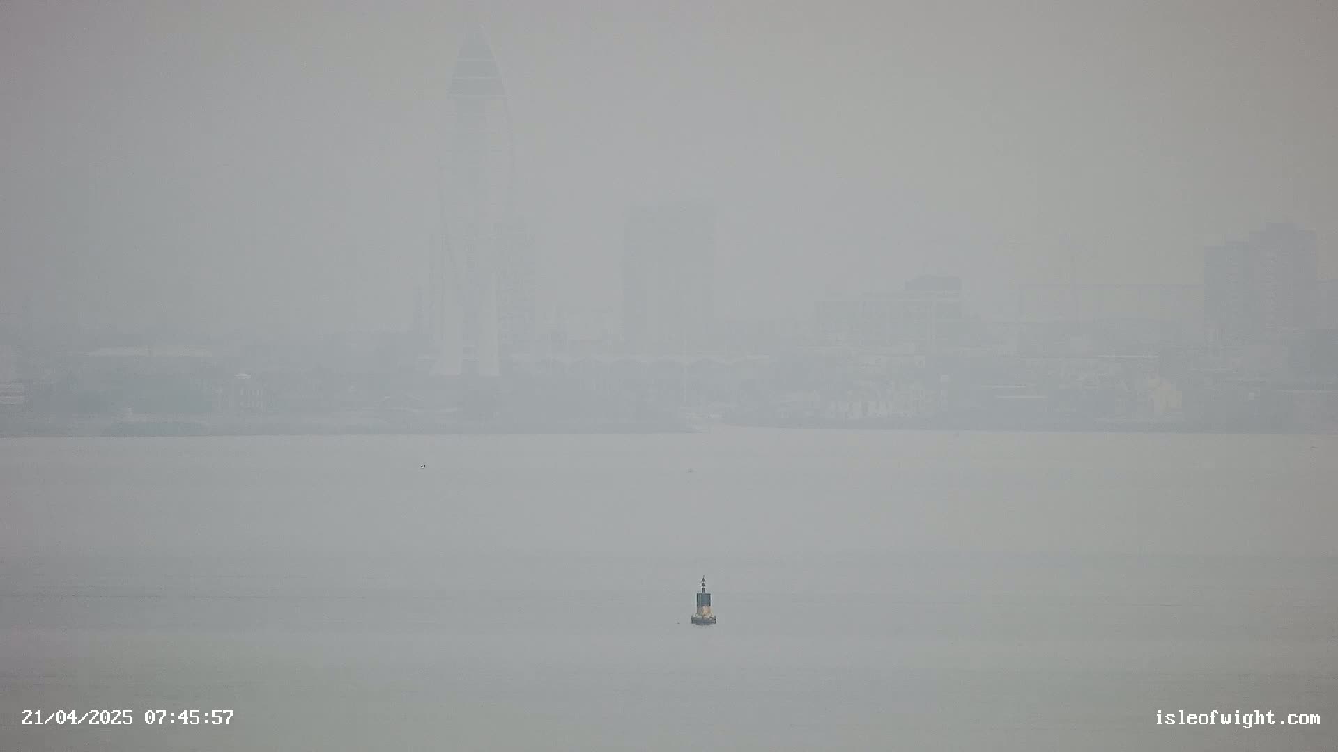 A hazy, distant cityscape is visible across a calm body of water, featuring a single marker buoy in the foreground.