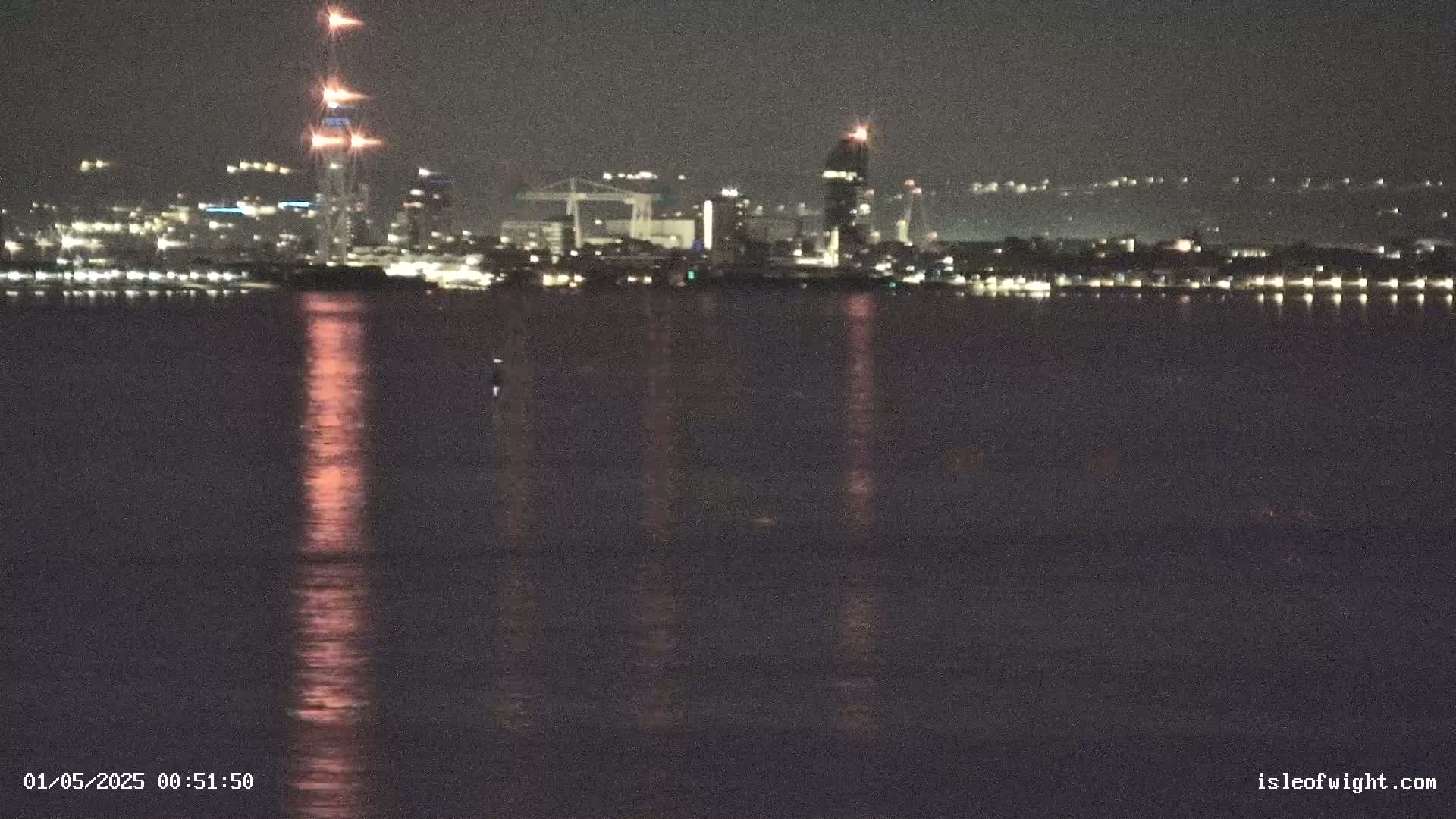 A nighttime view of a city skyline across a calm body of water, with lights reflecting on the surface.
