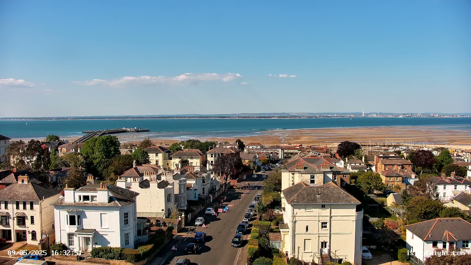 A sunny day overlooks a seaside town with houses lining a street leading toward a pier and expanse of ocean.